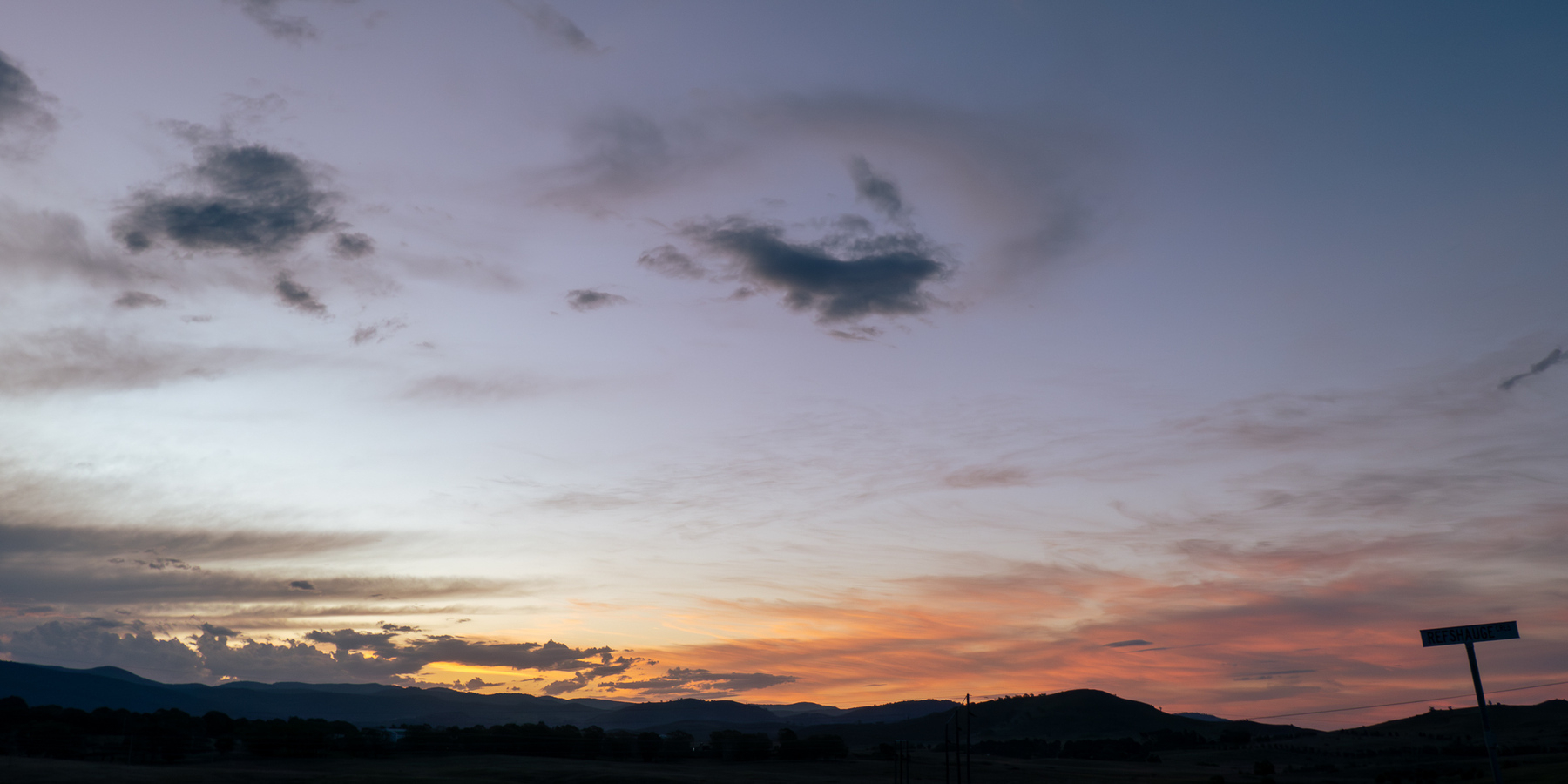 A sunset - an orange glow above some hills with a clear grey and blue sky above. A couple of grey clouds float high in the sky