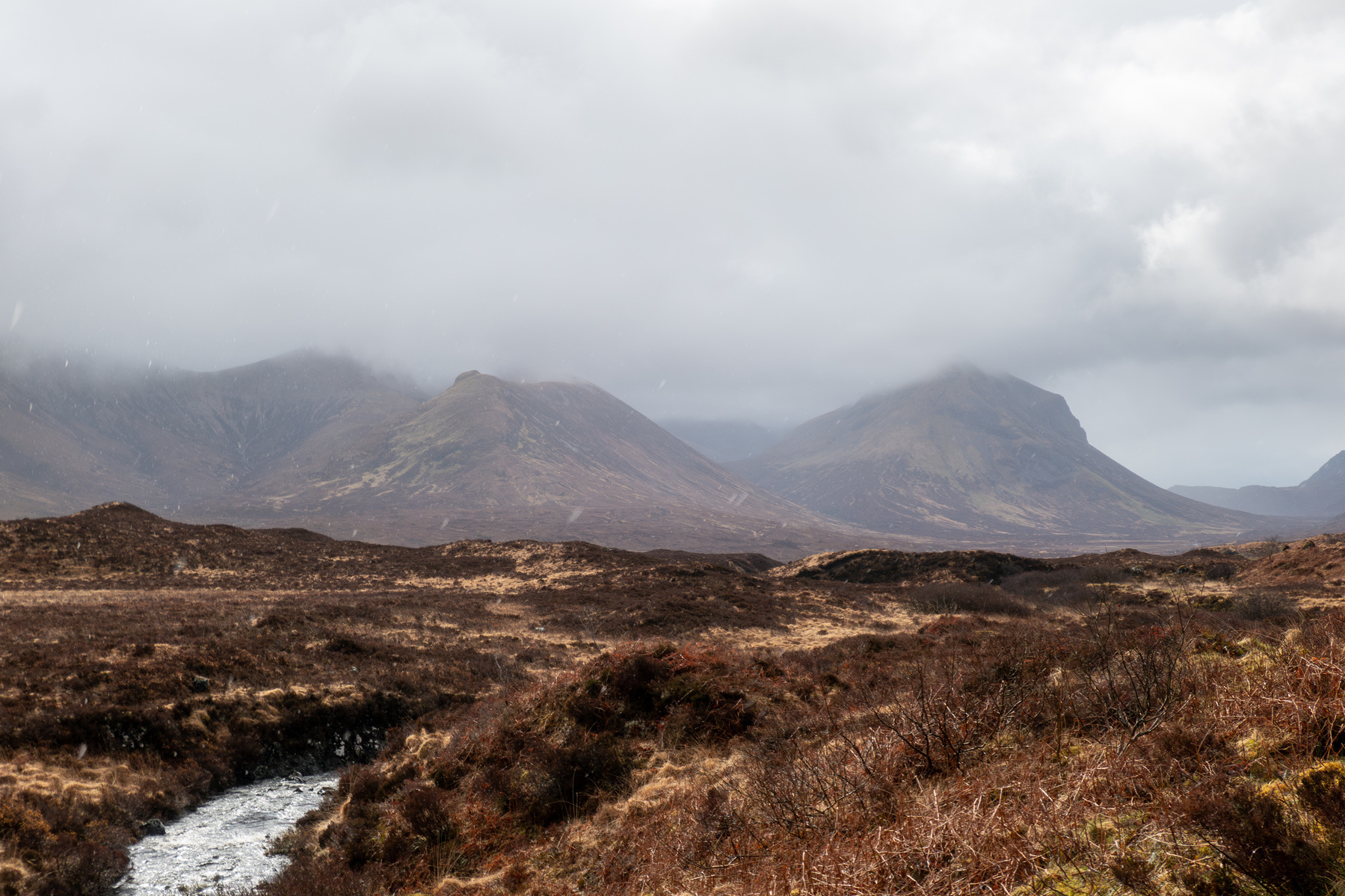 The Scottish Highlands - distant mountains covered in fog, a stream flowing through a field.