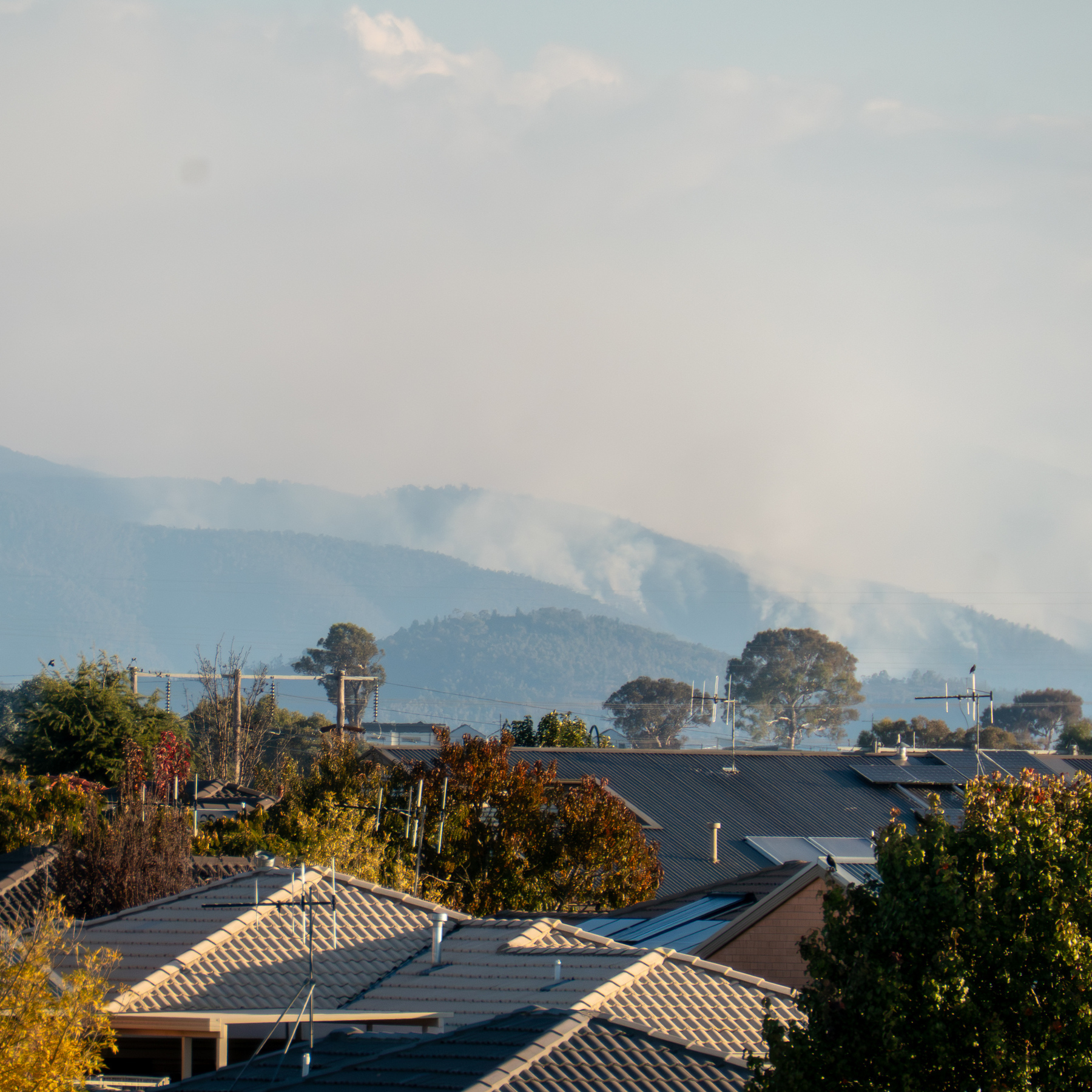 Smoke rising from mountains in the distance. Roofs of houses in the foreground.