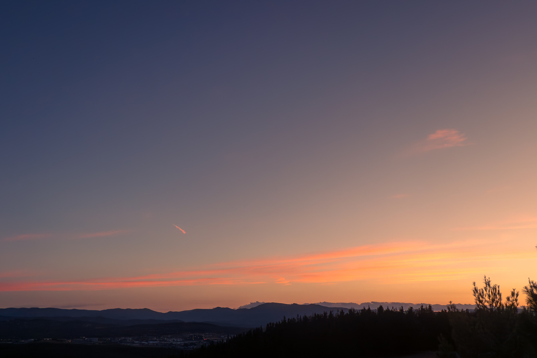 Orange and yellow glow with low clouds above the silhouettes of the mountains