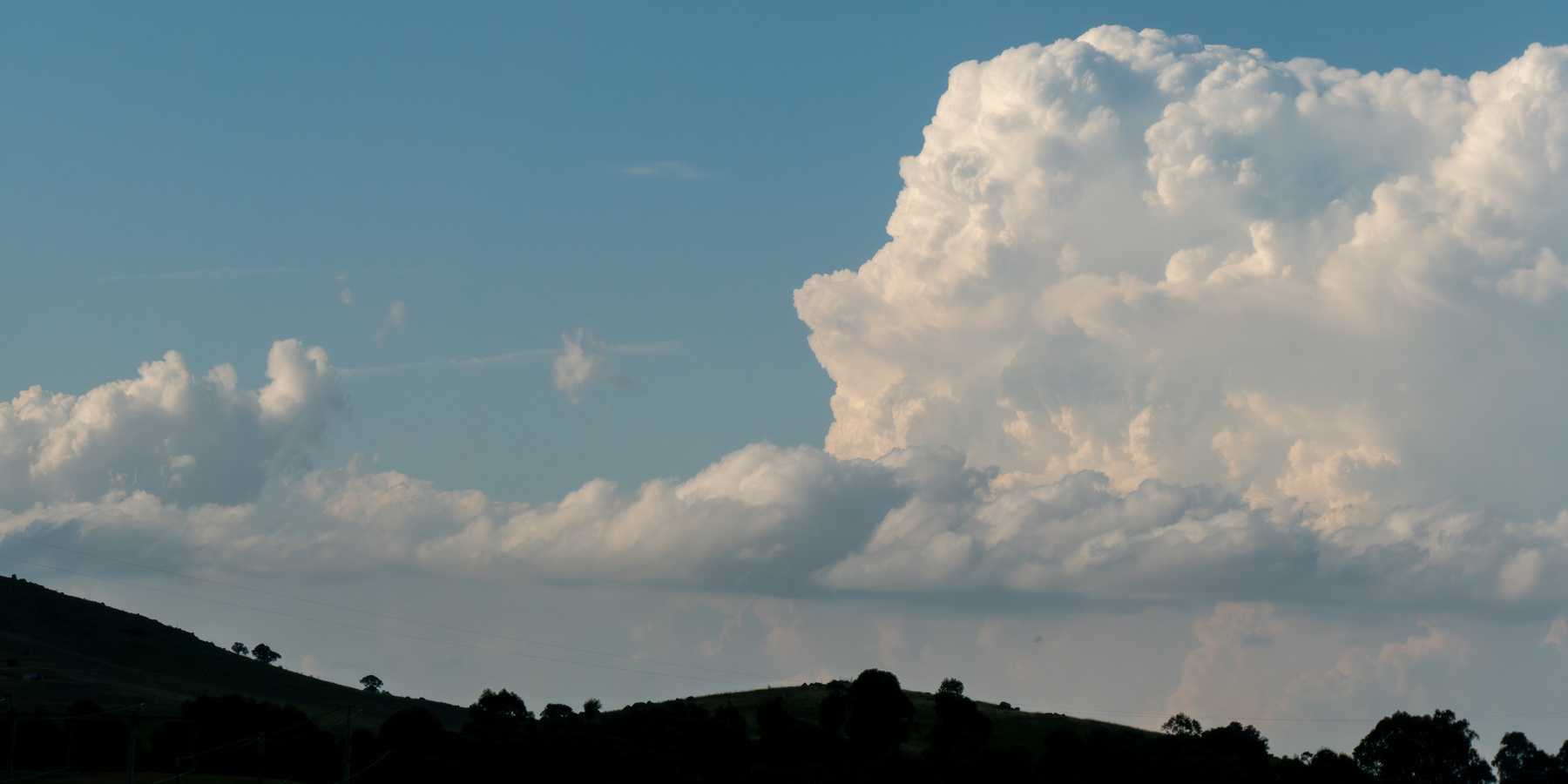 Some nice looking white clouds in a blue sky with the silhouette of some hills at the bottom.