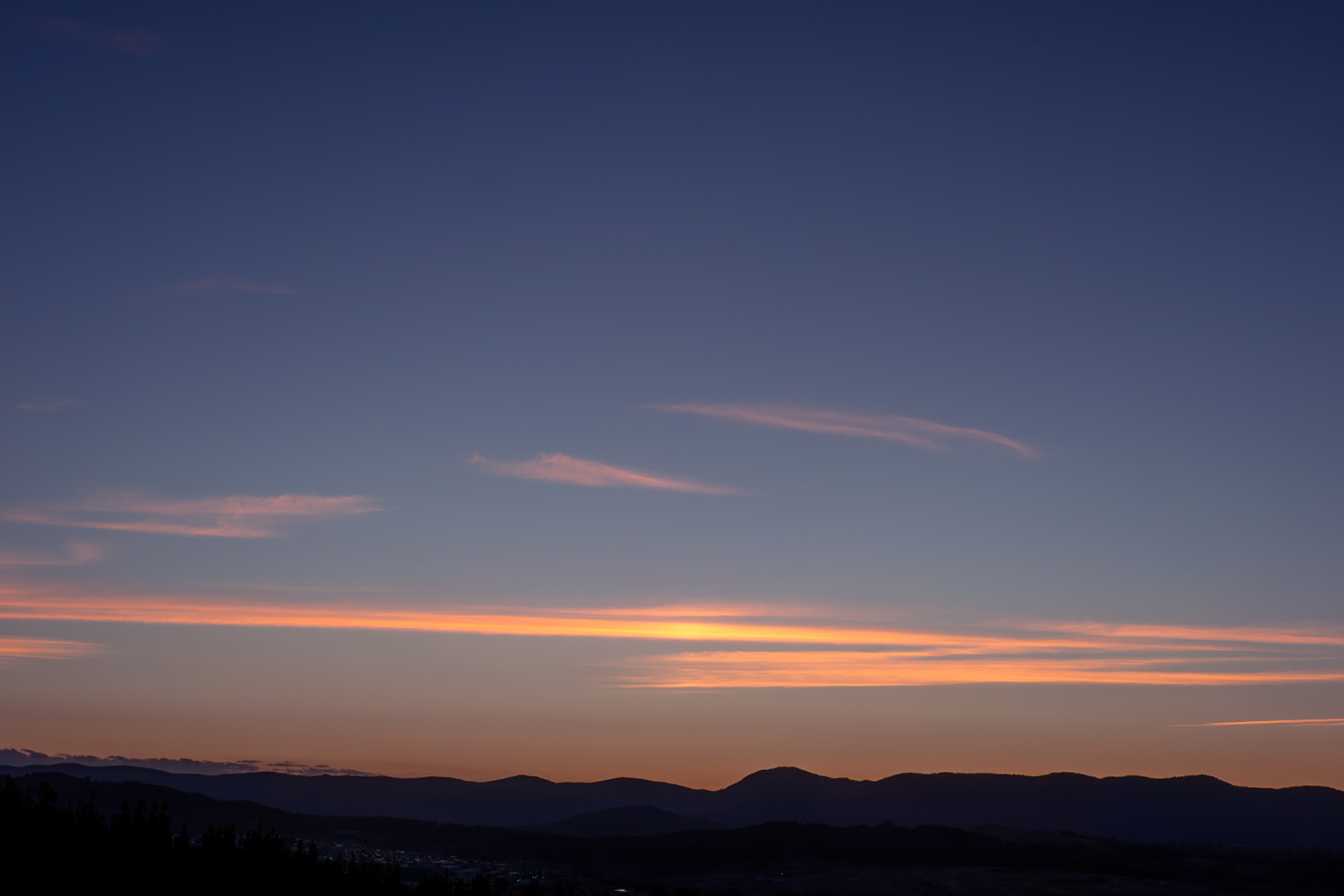 Streaks of yellow and orange clouds in a deep blue sky just above the horizon