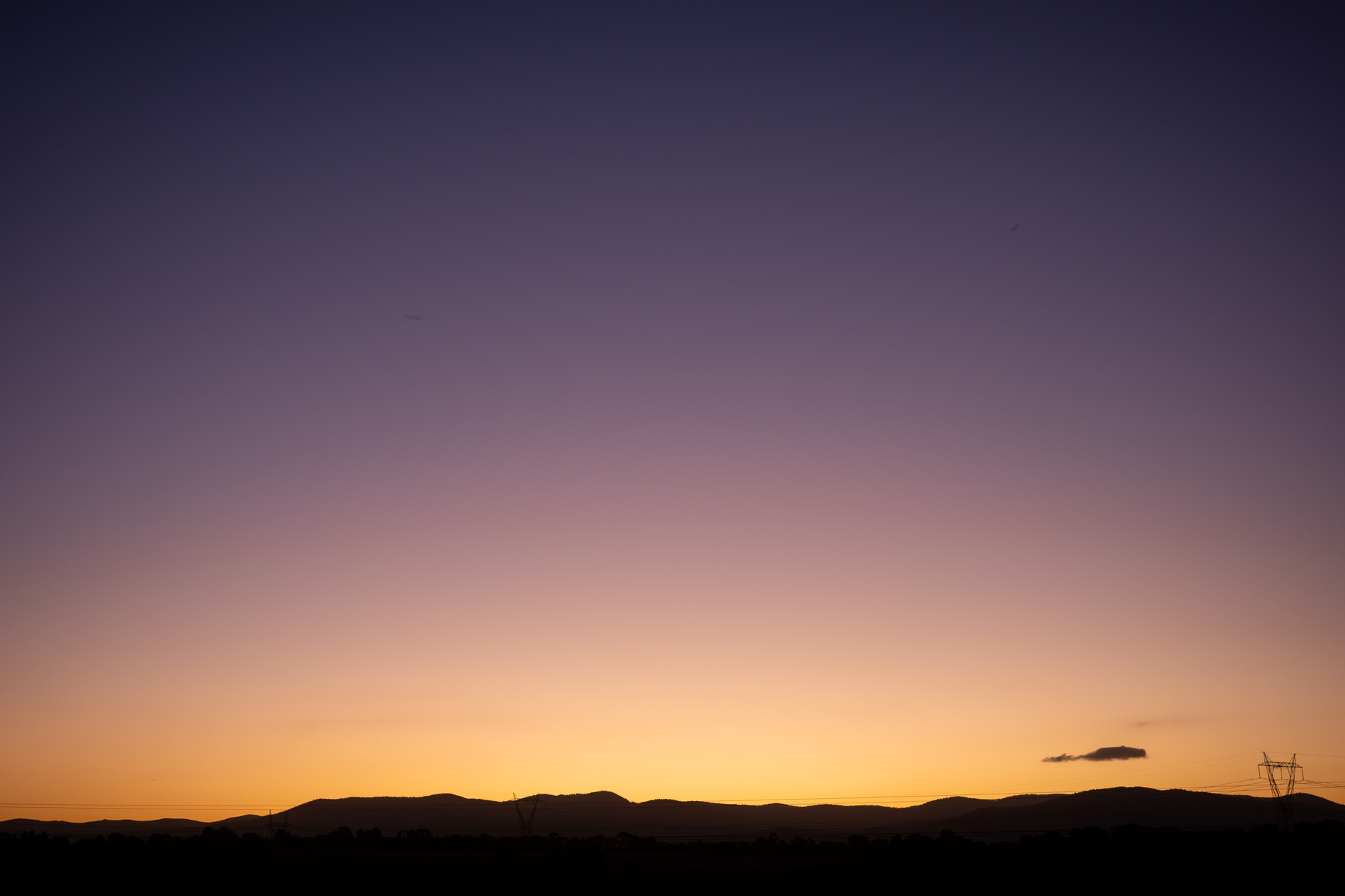 A sunset with an almost cloudless sky. Yellow to orange to purple gradient above the silhouette  of the mountains.