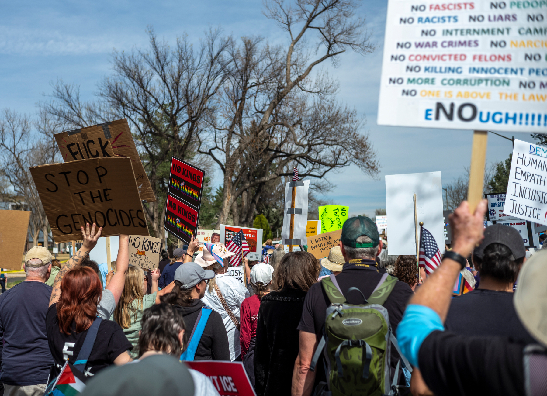 photo of an anti-trump rally with many people in the scene; focus of the image is a person holding a poster that says STOP THE GENOCIDES