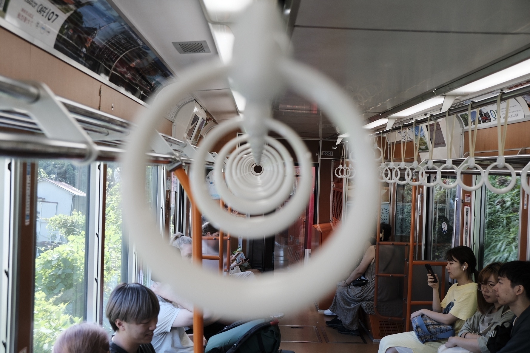 From the inside of a train, and you see lots of rings to hold on to, shot from the side. White rings. Wooden interior around, people sitting on the chairs and staring at their phones 