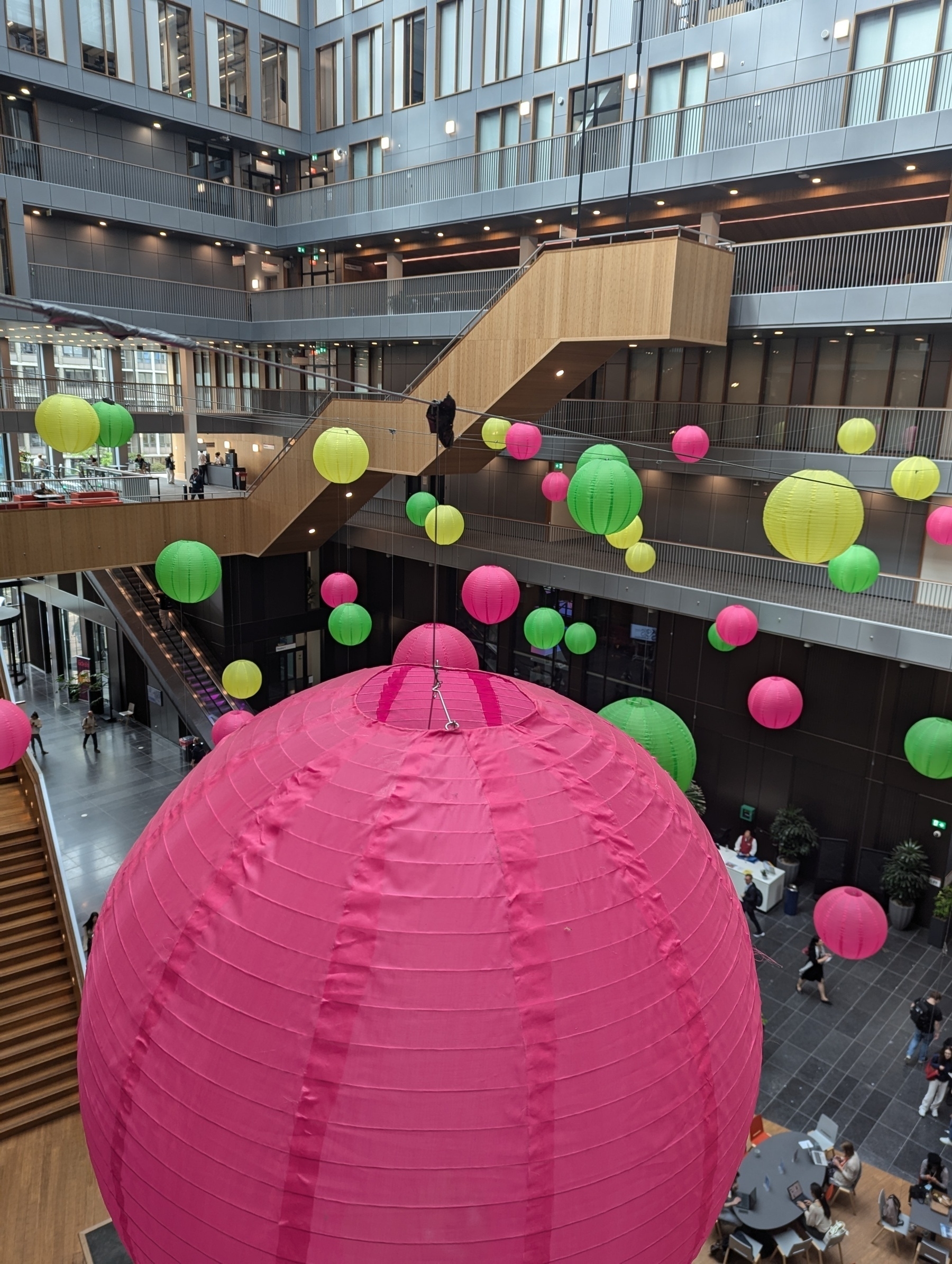 Photography from the inside of the new main building of free university, Amsterdam. You see wooden stairs, colourful light balloons, and a large hall below