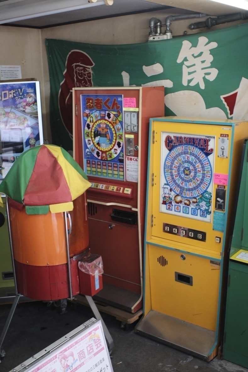 A snapshot of old arcade game machines, of which you find many in tiny Osaka alleys. Den den town. Colourful games on display with Japanese writing on the wall—in the background. &10;&10;Osaka is much more unruly and even dirty at times, compared to the other big cities in Japan, which indicates more freedom. Queerness, a bit? But liveability in general? Em, no, especially on a global scale &10;