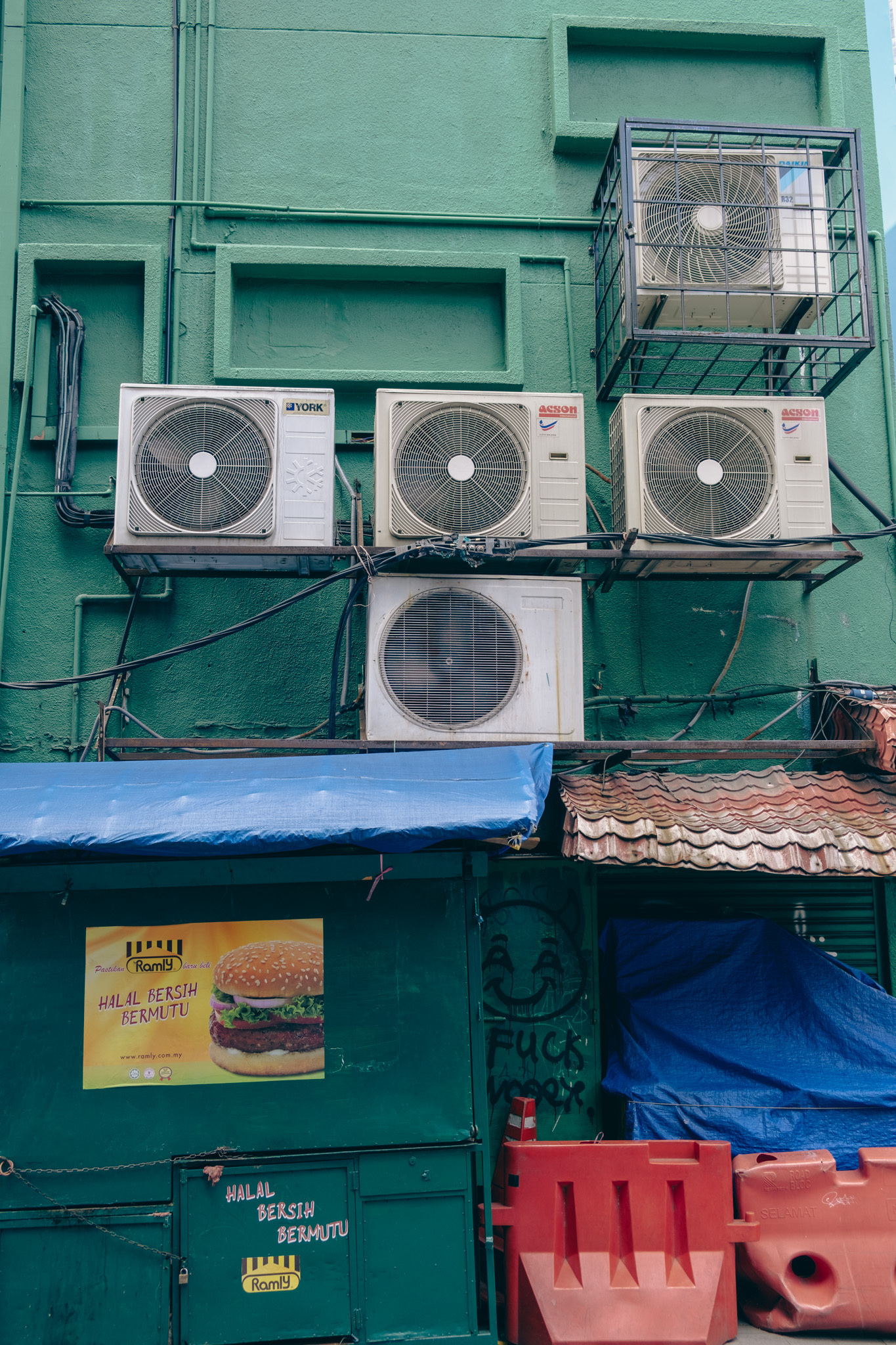 An image of air condiction fans outside a restaurant building in KL, Malaysia. White fans in front of a green wall, a little bit of posters and construction material on the lower part of the image