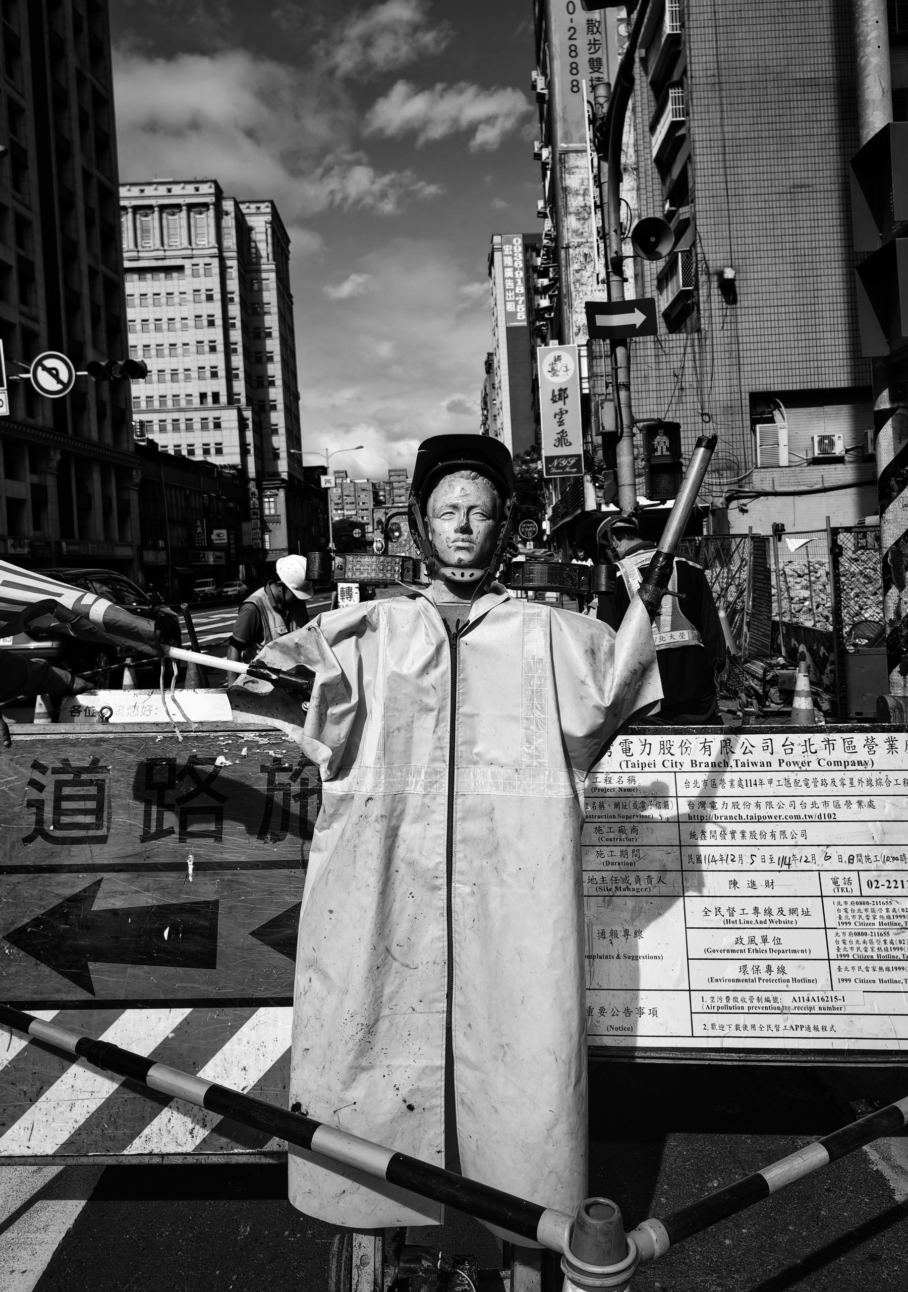 A construction puppet directing pedestrians, a black and white photo of a very busy and colourful construction scene 