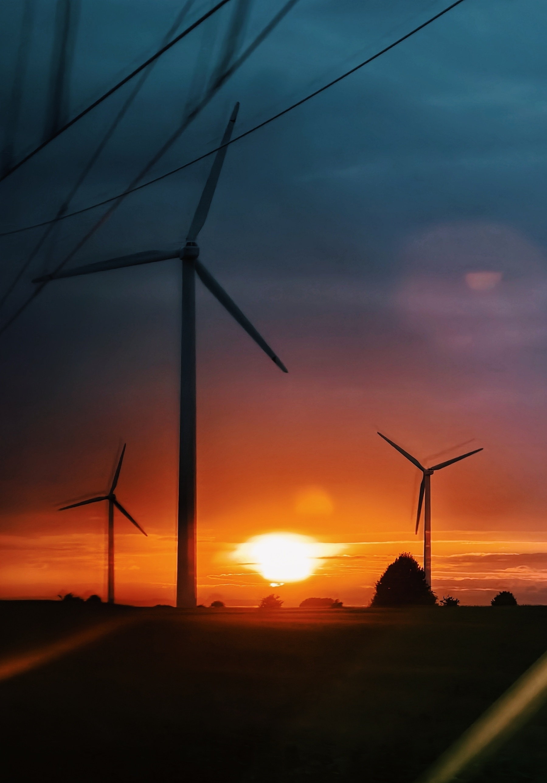 Sunset shot through the window of a driving train, right into the sun, a green turned black field in the front, some wind power around 