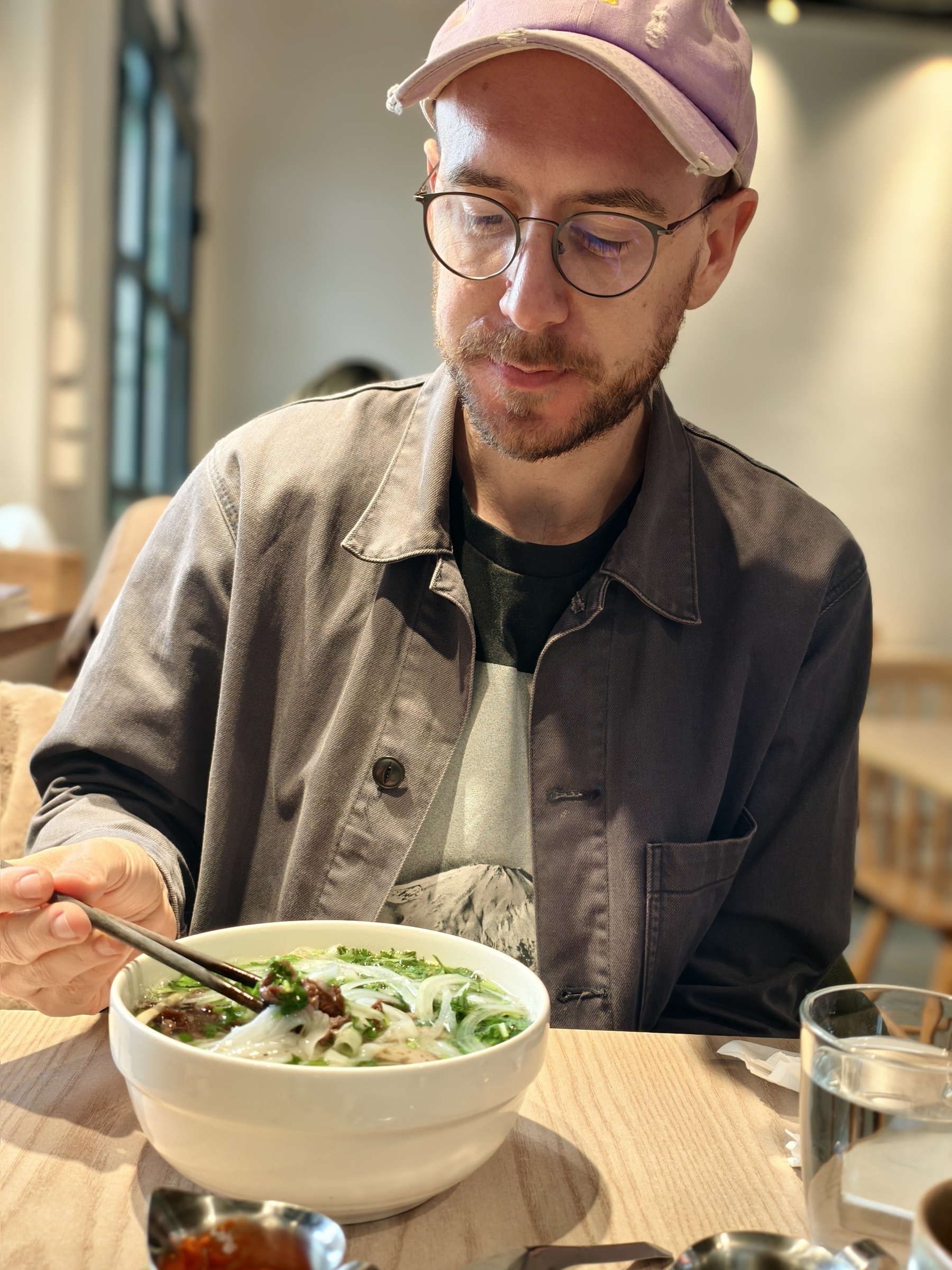 Me, the poster, digging a pho, digesting the hot sauce I always added on top. You see a man with a cappie and glaces looking down at a soup, grabbing food with chop sticks