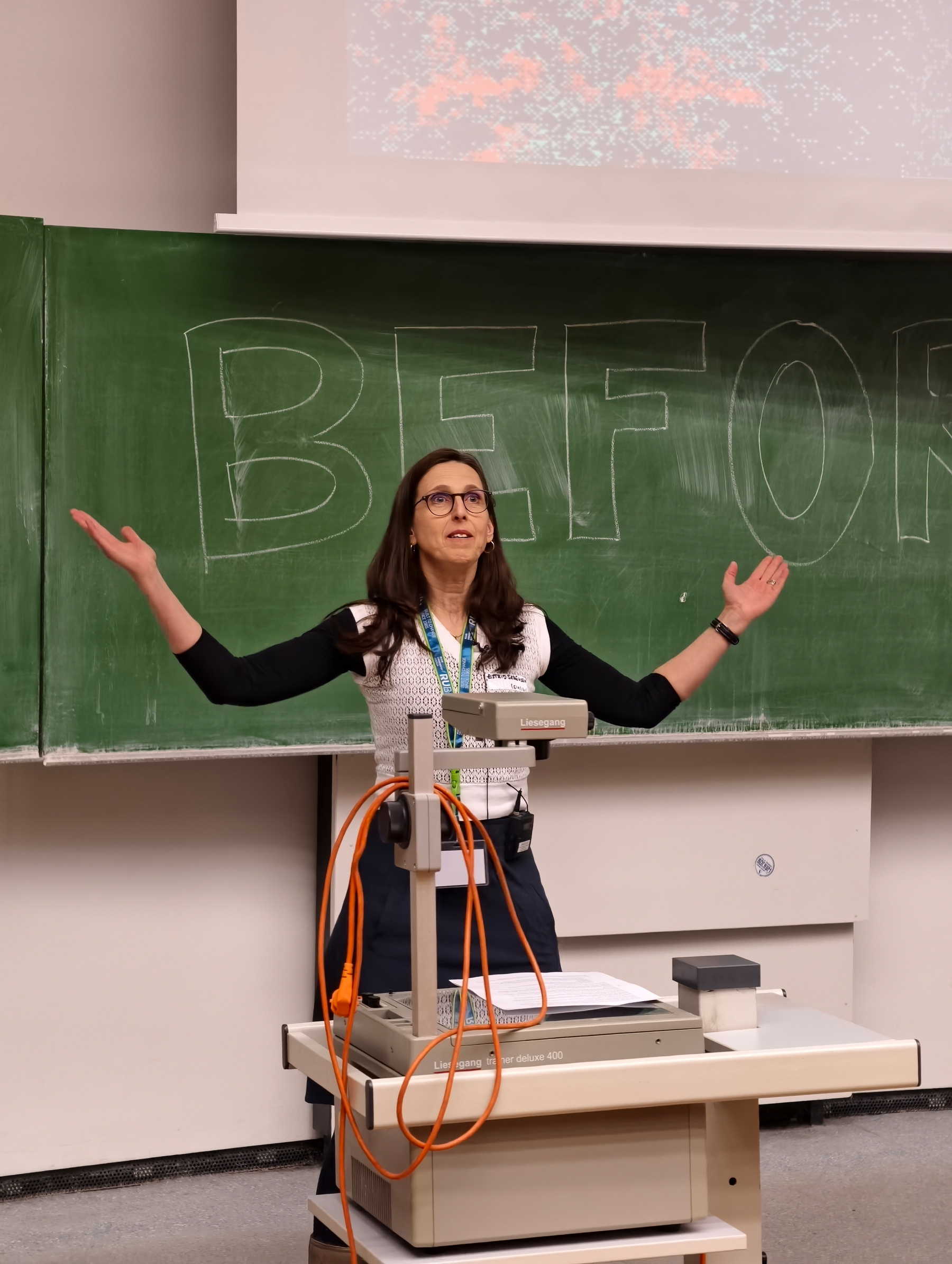Welcome address by Estrid. A woman with arms spread out standing before a green chalk board