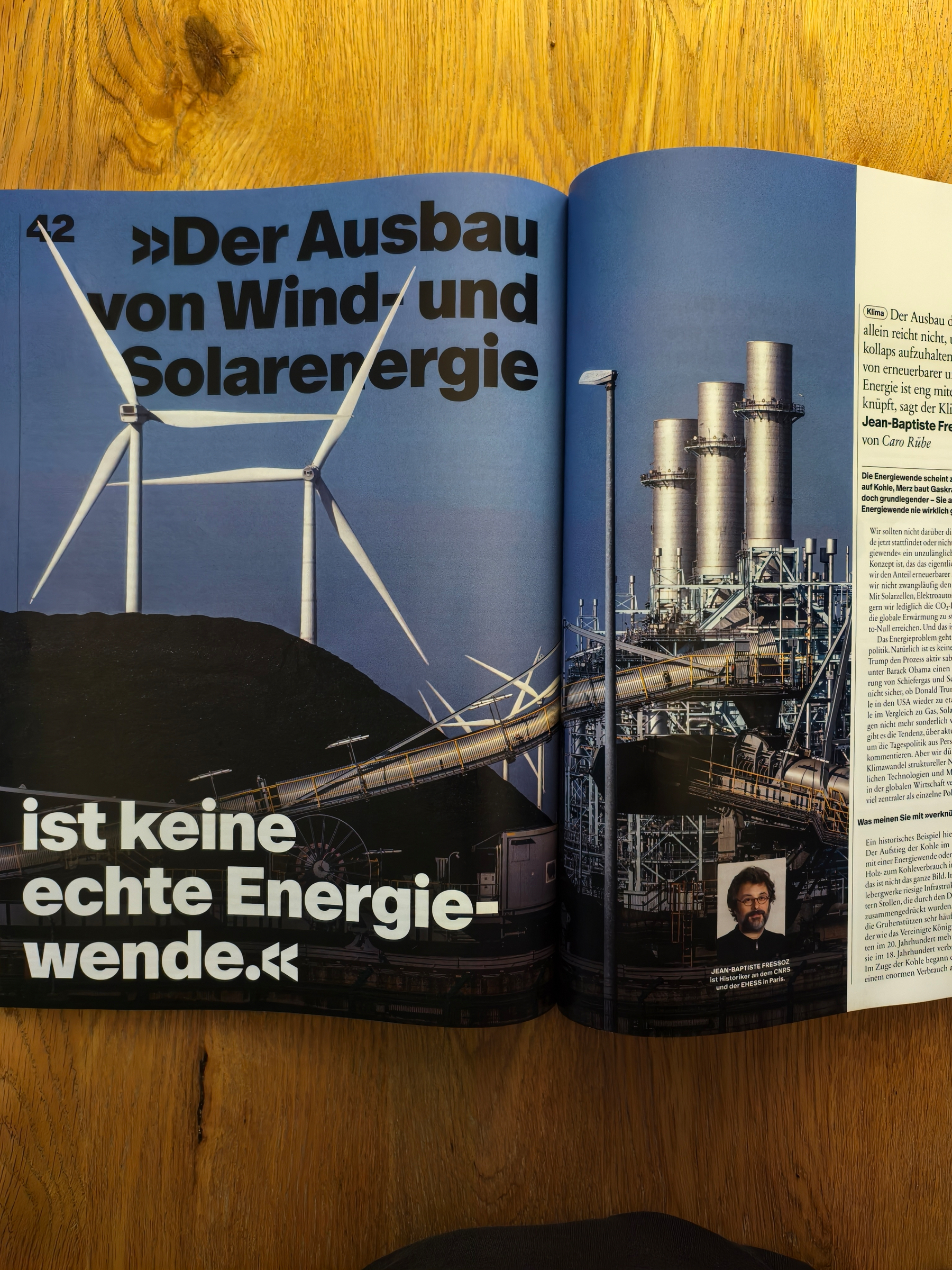 Foto auf einem Holztisch: eine Seite des Surplus-Magazins mit Windkraftanlagen abgebildet neben fossiler Infrastruktur. Titel: Der Ausbau von Wind- und Solarenergie ist keine echte Energiewende". Provokant 