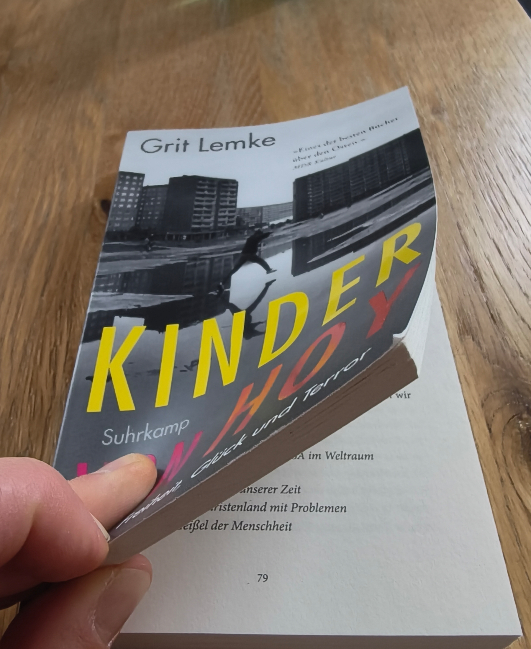 Cover des Buchs, ein schwarz weiß Shot eines Kindes, das inmitten von Neubauten über Pfützen springt. Der Titel in Gelb und Lila