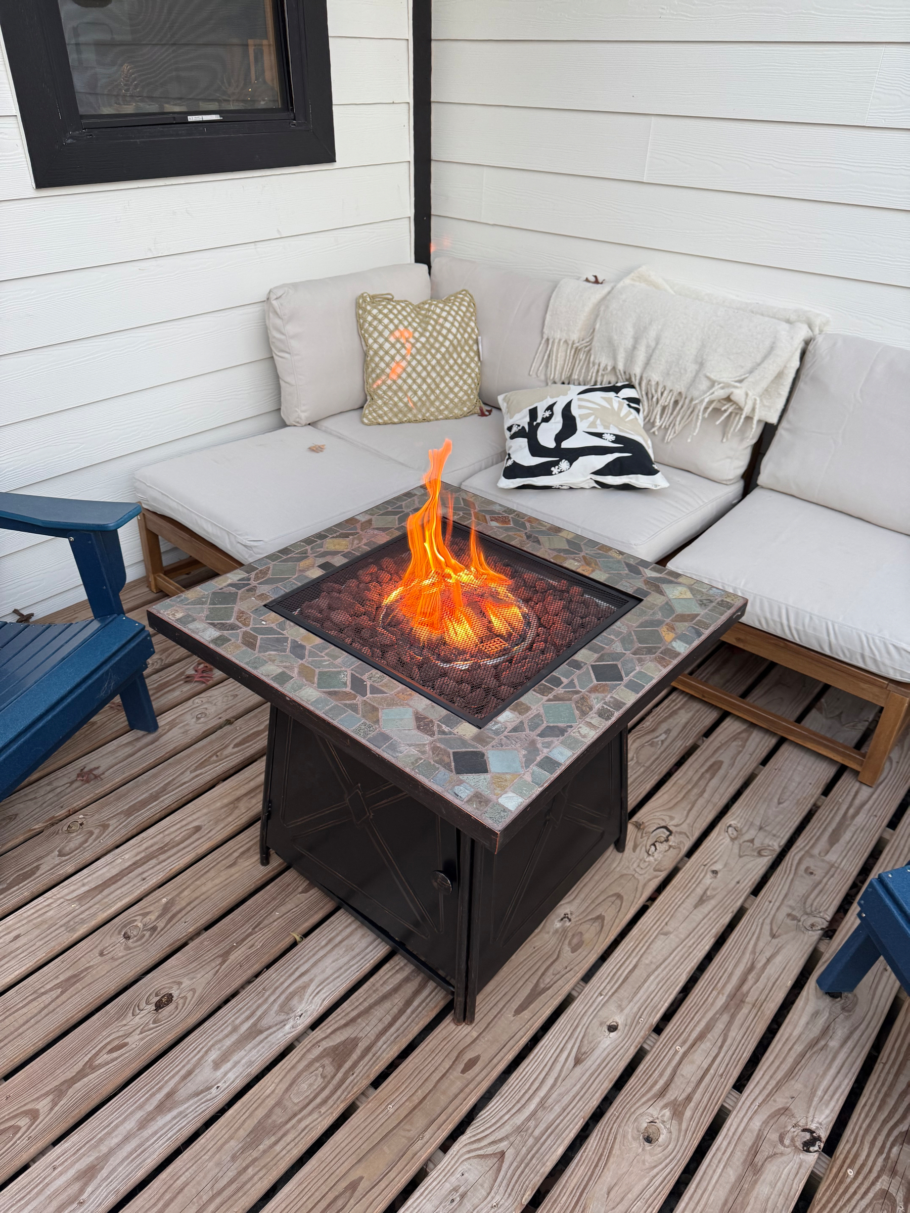 A cozy outdoor seating area features a fire pit table surrounded by cushioned chairs on a wooden deck.
