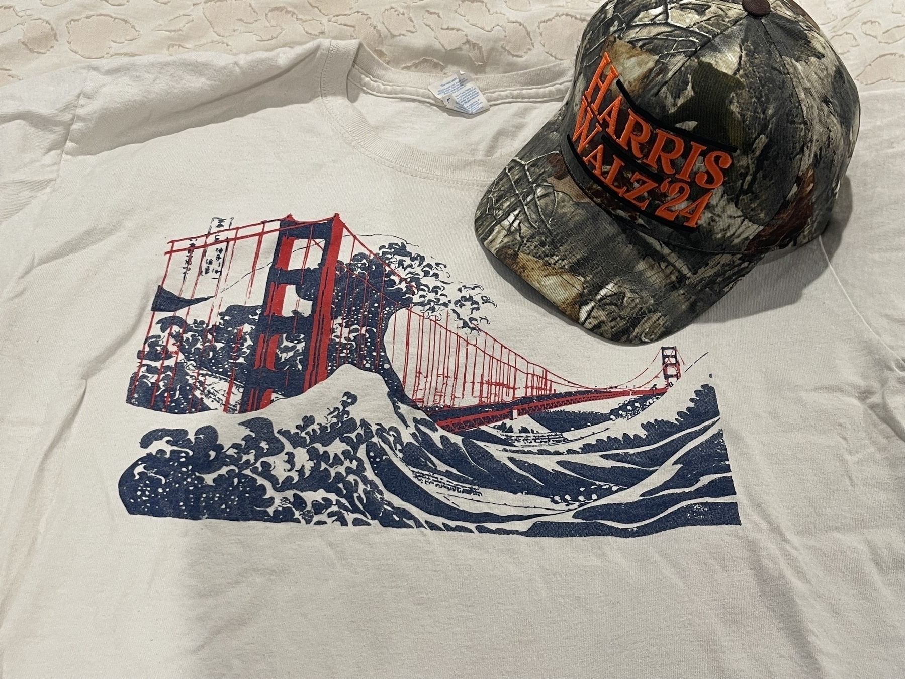 A T-shirt features a blend of the Golden Gate Bridge and the famous Japanese painting of “wave off Kanagawa” design, accompanied by a camouflage baseball cap with text reading "HARRIS" and "WALZ ‘24".