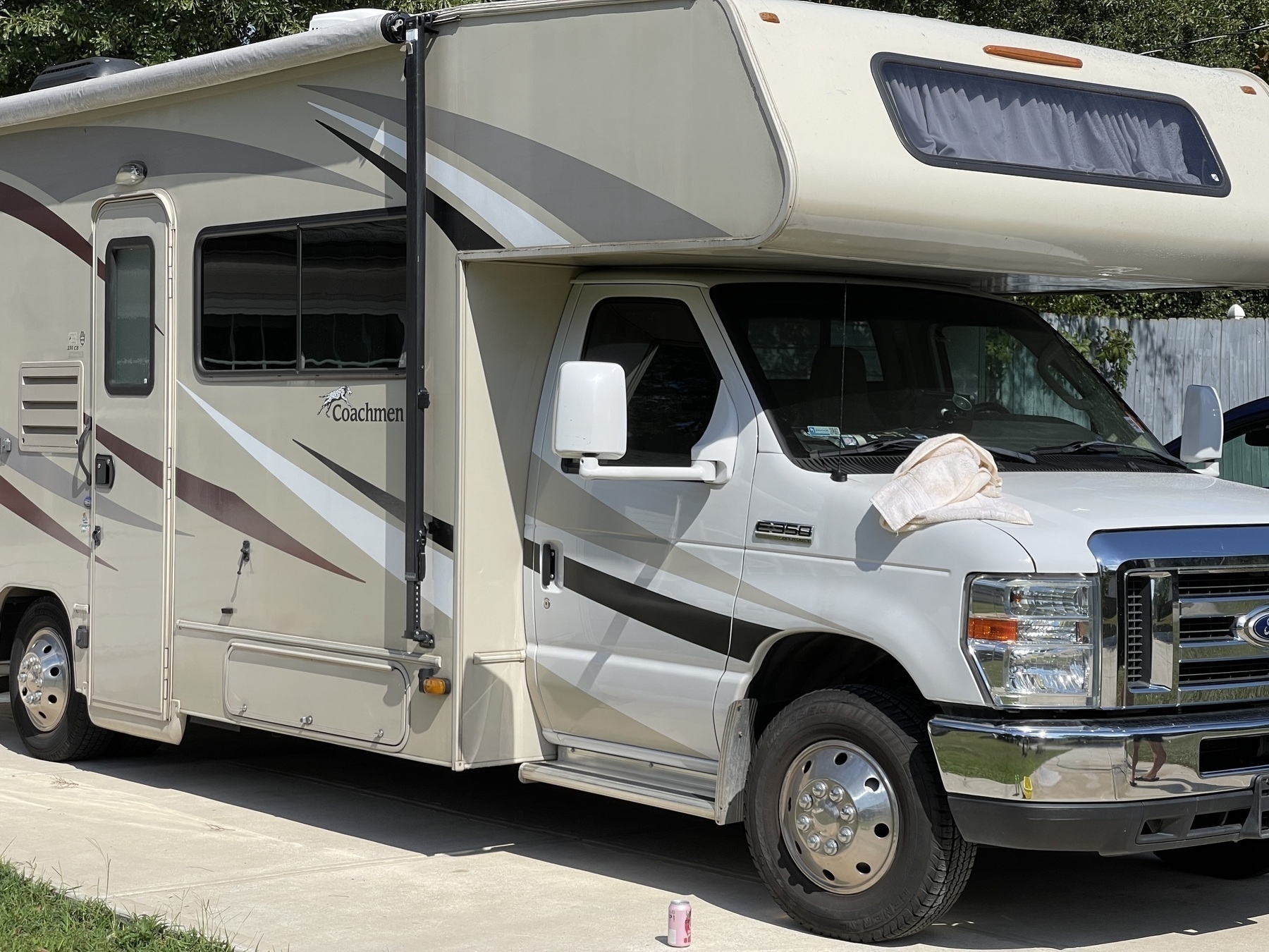 A motorhome is parked on a driveway with a can on the ground and a towel on the hood.