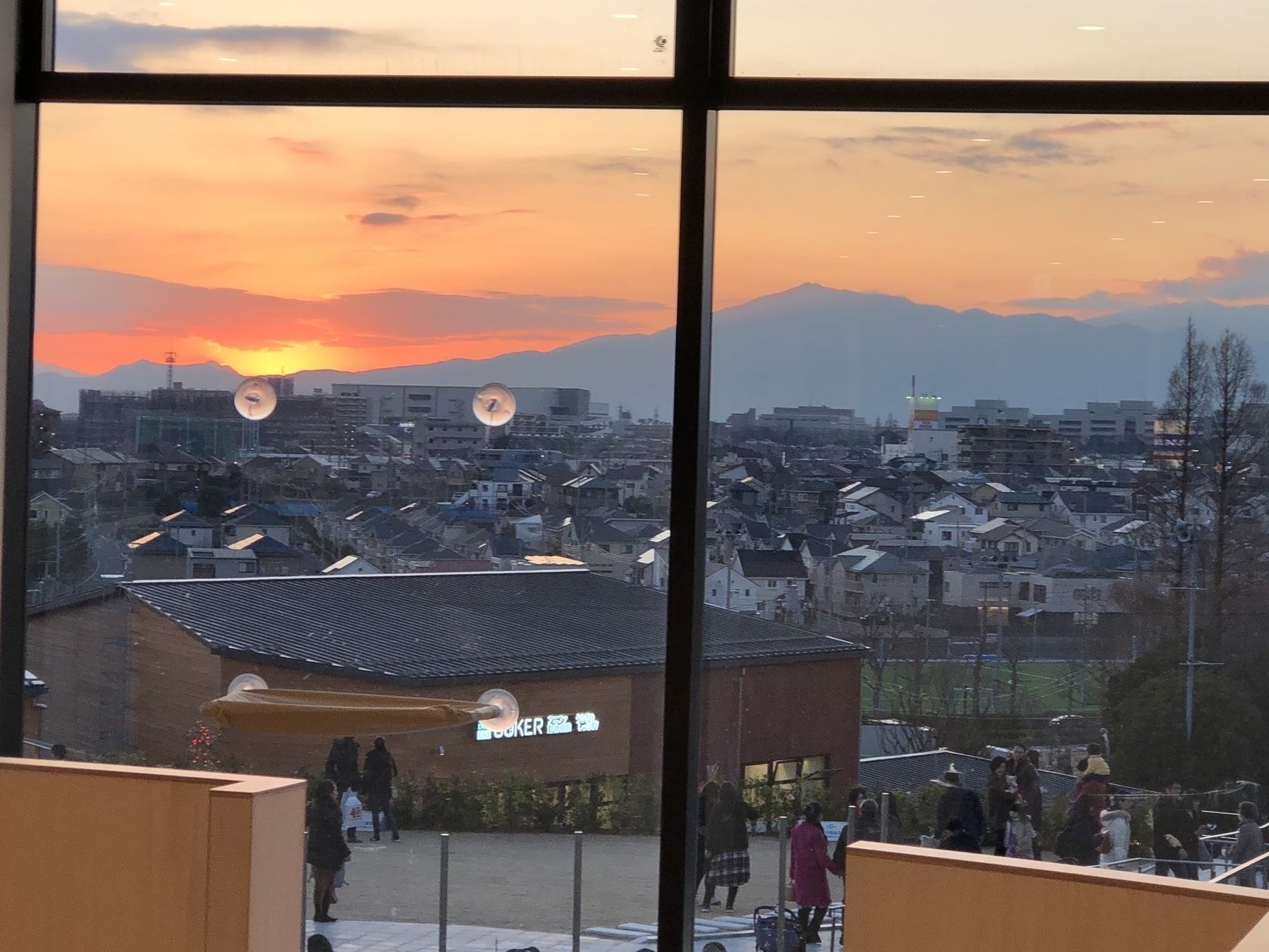 A sunset view over a suburban landscape outside Tokyo is seen through a large window, with buildings and distant mountains in the background.