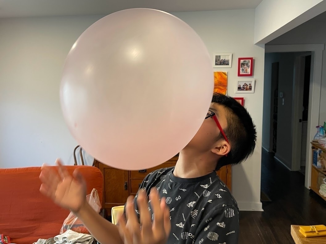 My then 13 year old son is captured in a playful moment, blowing a large, pink bubble gum bubble. The bubble is so big it almost obscures his face, highlighting the fun and lighthearted nature of the activity