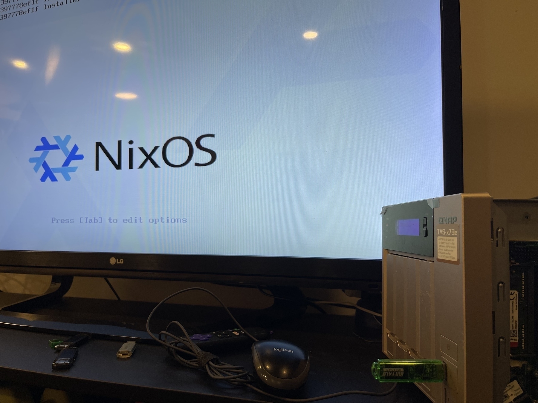 A computer setup with a monitor displaying the NixOS logo and a collection of peripherals on the table.