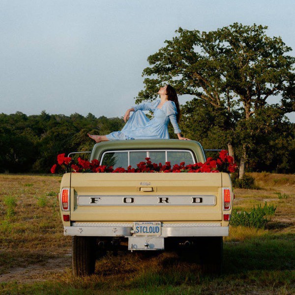 Album cover of Saint Cloud by Waxahatchee, showing a woman sitting on the roof of a pick-up truck with red flowers in the bed of the truck.