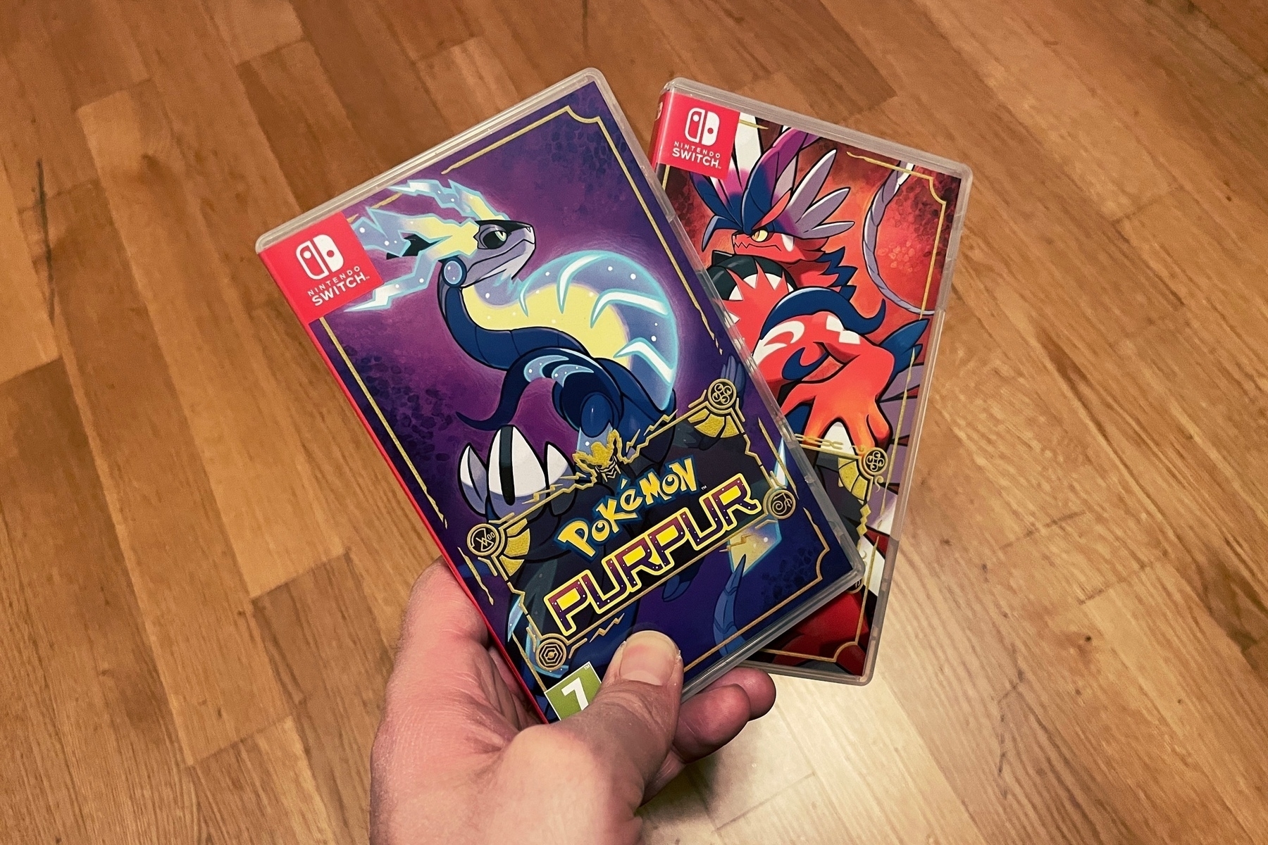 Hand holding physical copies of Pokémon Violet and Scarlet