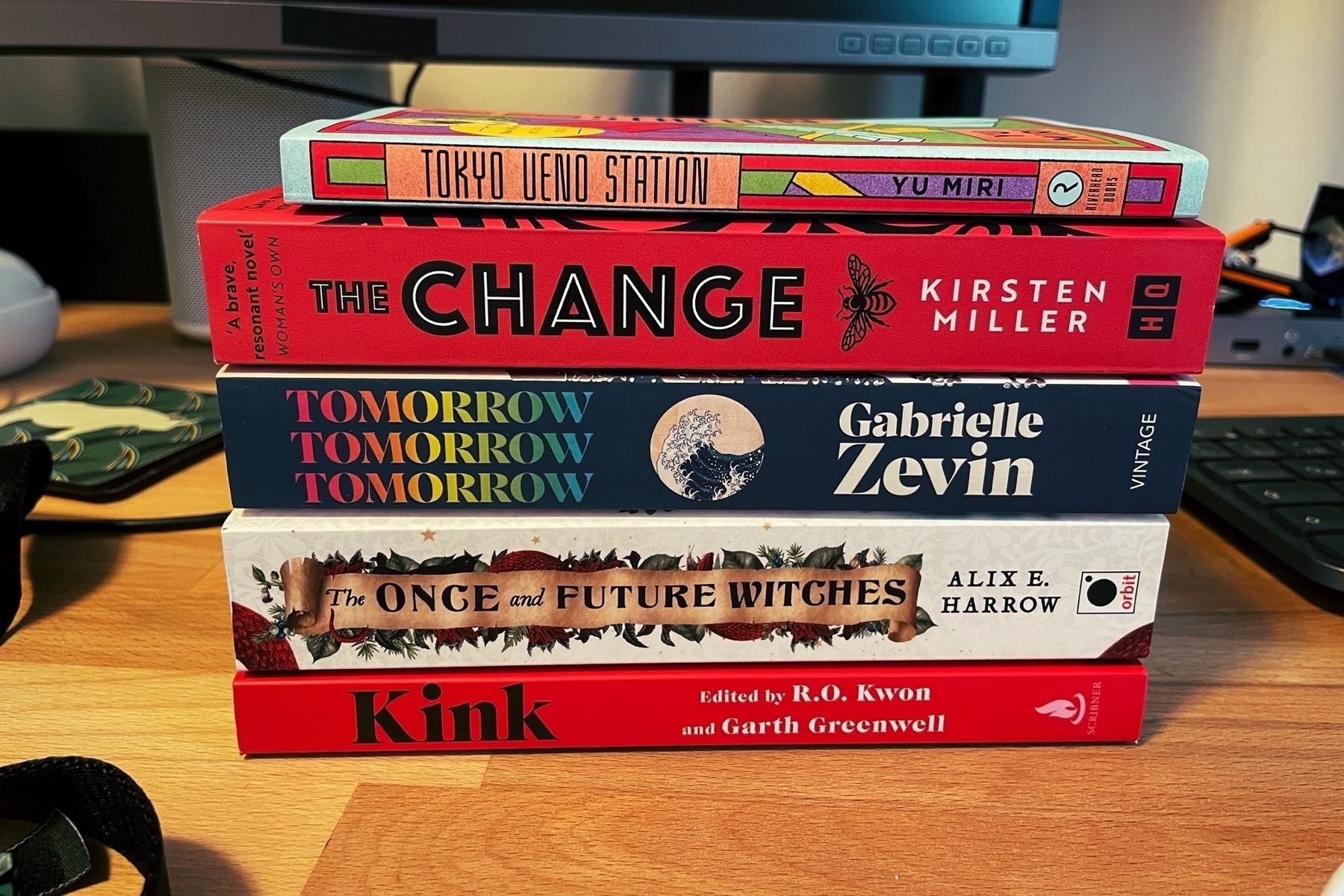 Stack of books on a desk: Kink, The Once and Future Witches, Tomorrow Tomorrow Tomorrow, The Change, and Tokyo Ueno Station.