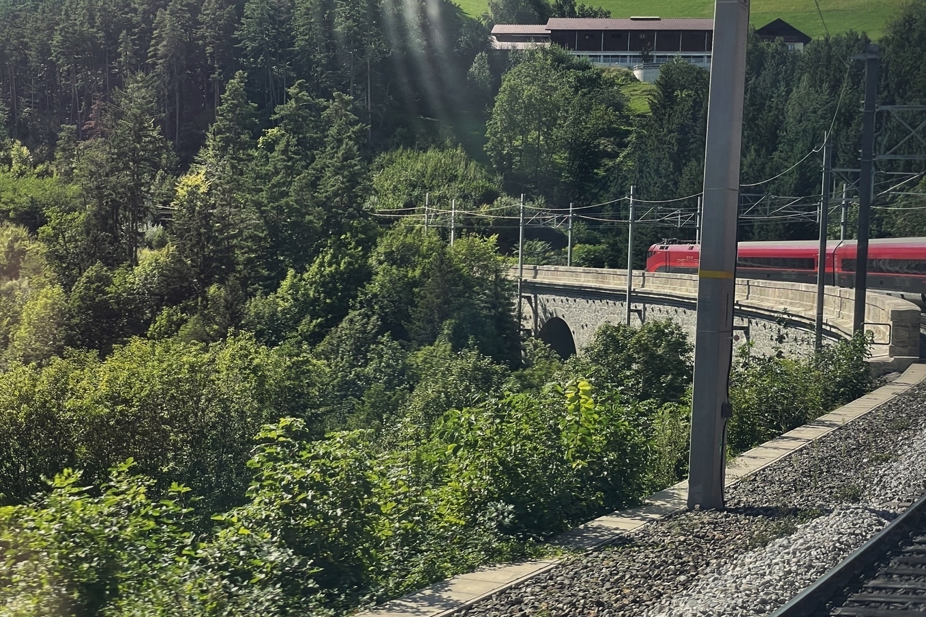 Train traveling through a bend, so you can see the preceding wagons, currently traveling over a stone bridge, lots of green and hills in the background