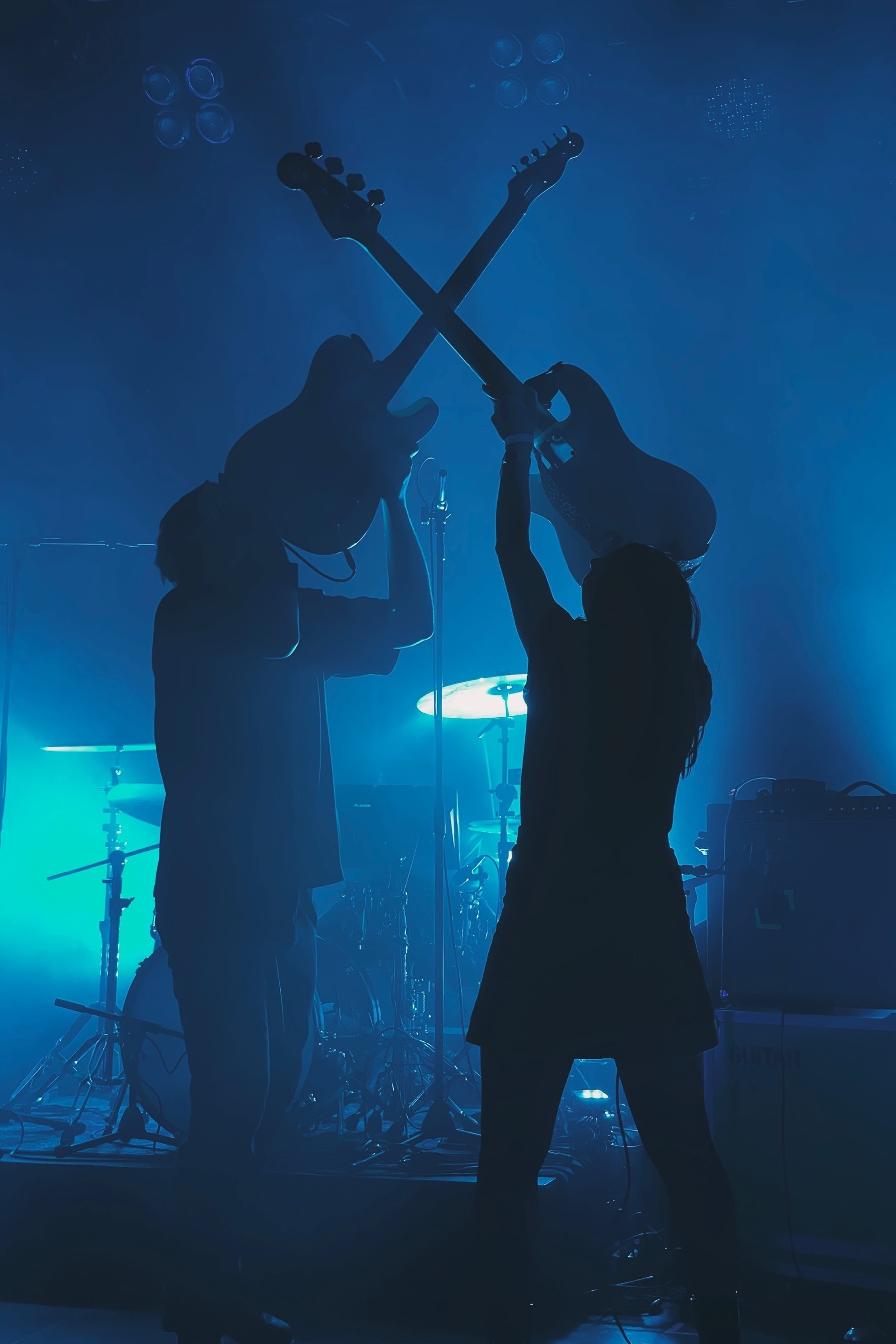 Guitarist and bassist holding their instruments up to form a X; the light is blue and green