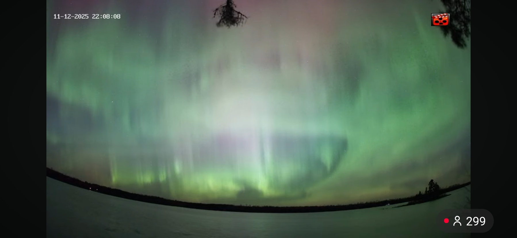 Screen view of a night sky with patches of green. White, and red across a fisheye horizon on a lake 