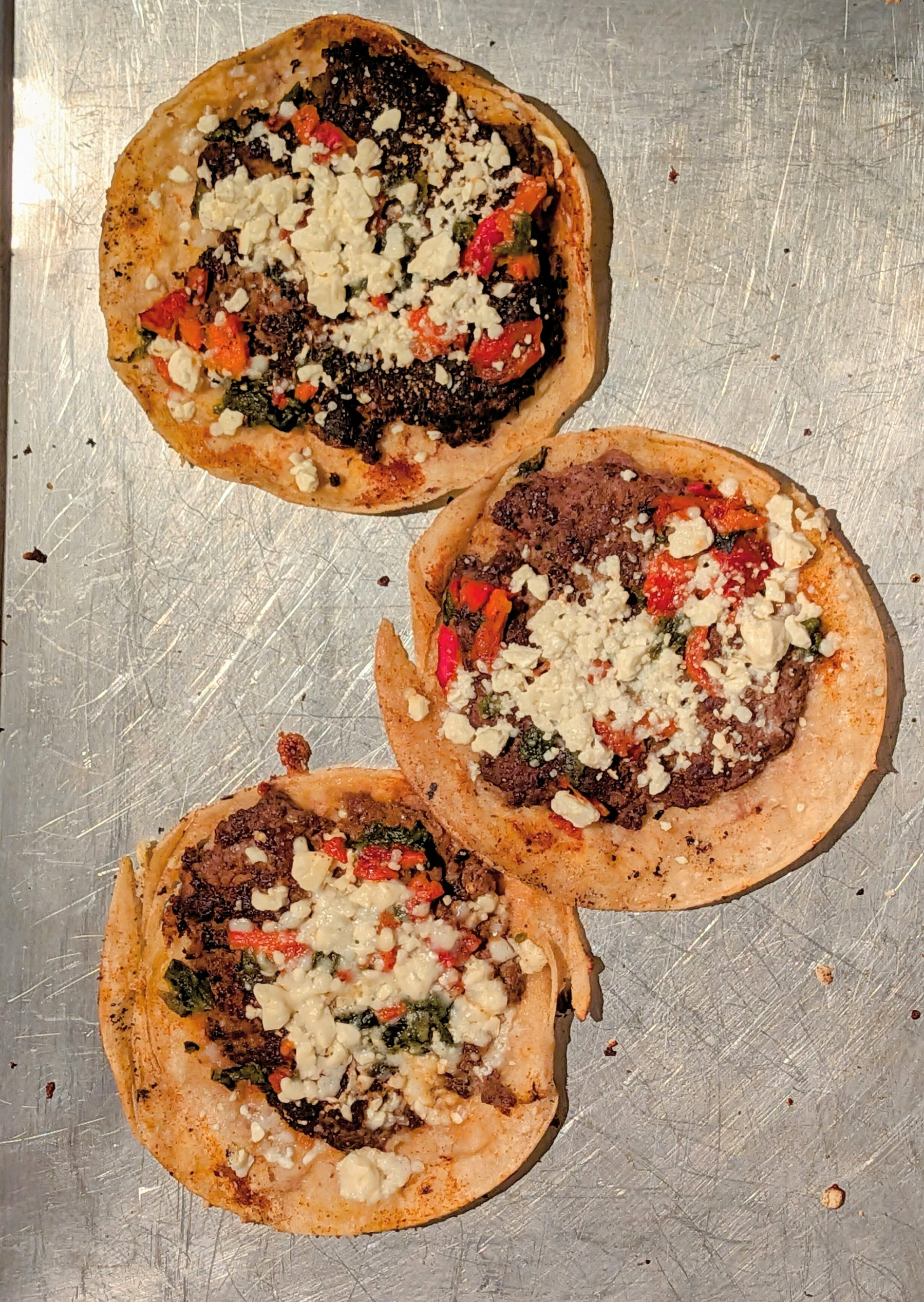 Three flat tacos with fried beef topped with white cheese crumbles.