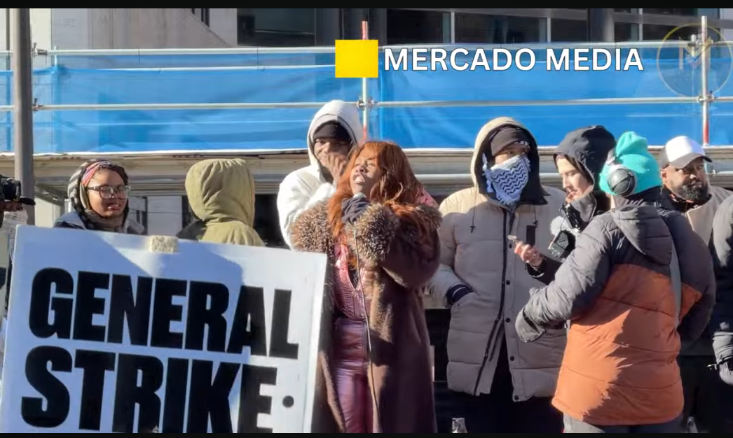 Group of people dressed for cold weather outside with a sign reading GENERAL STRIKE 