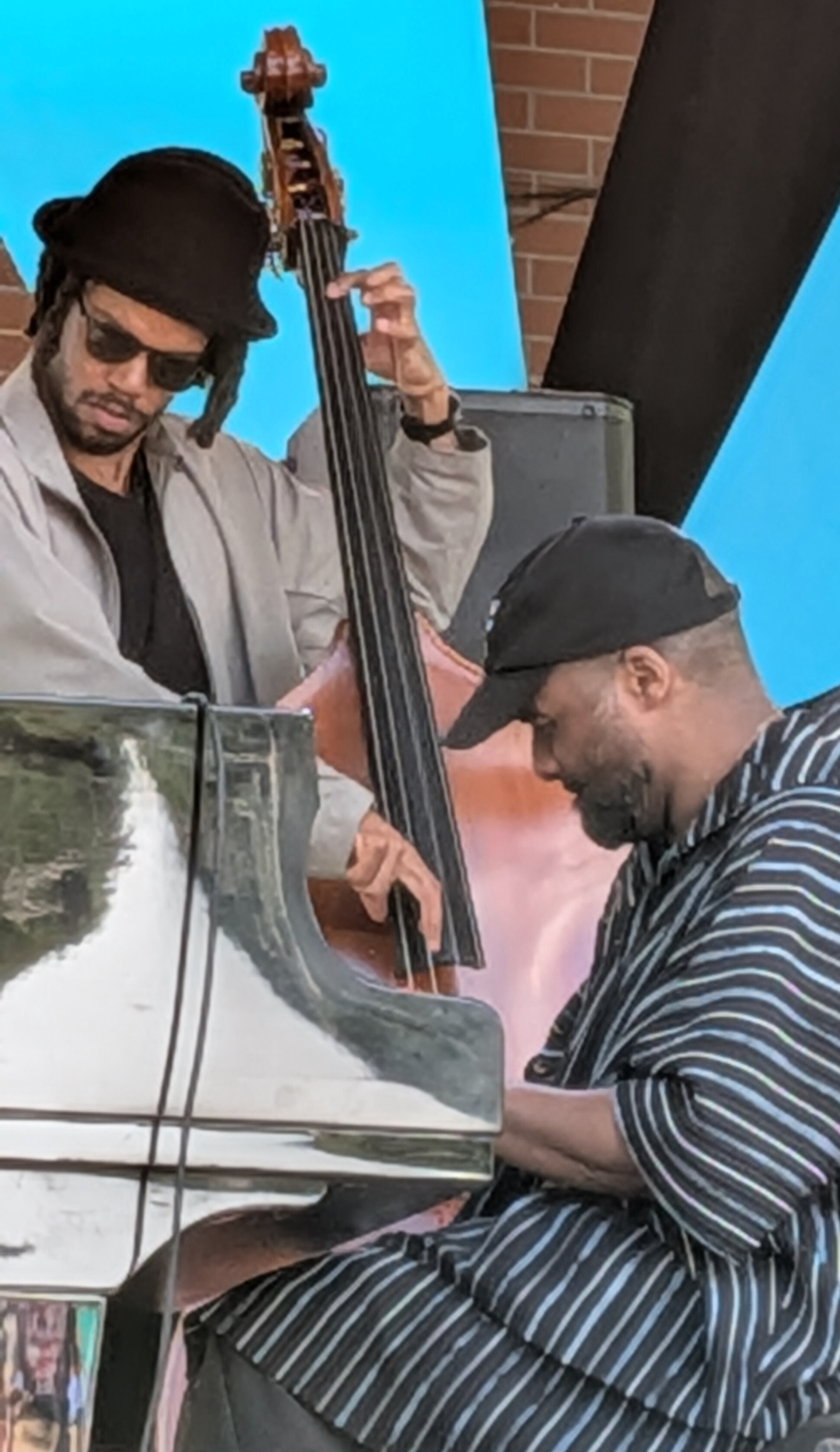 Man playing piano seen from side and another behind playing contra bass, at a jazz festival immersed in playing their music&10;