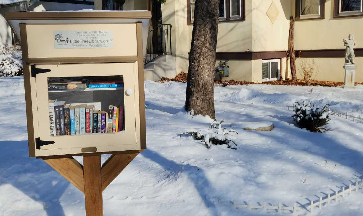 Sunny winter scene of box of Little Free LIbrary books on a wooden post in front of a house