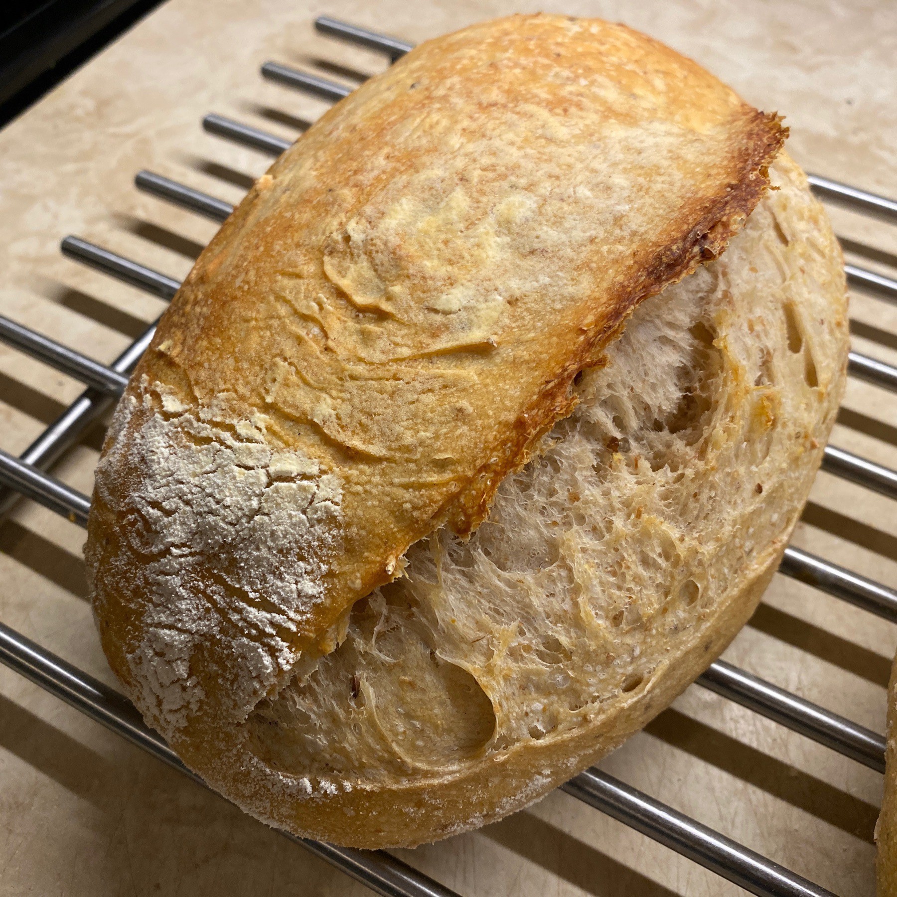 Sourdough bread loaf cooling on metal rack.