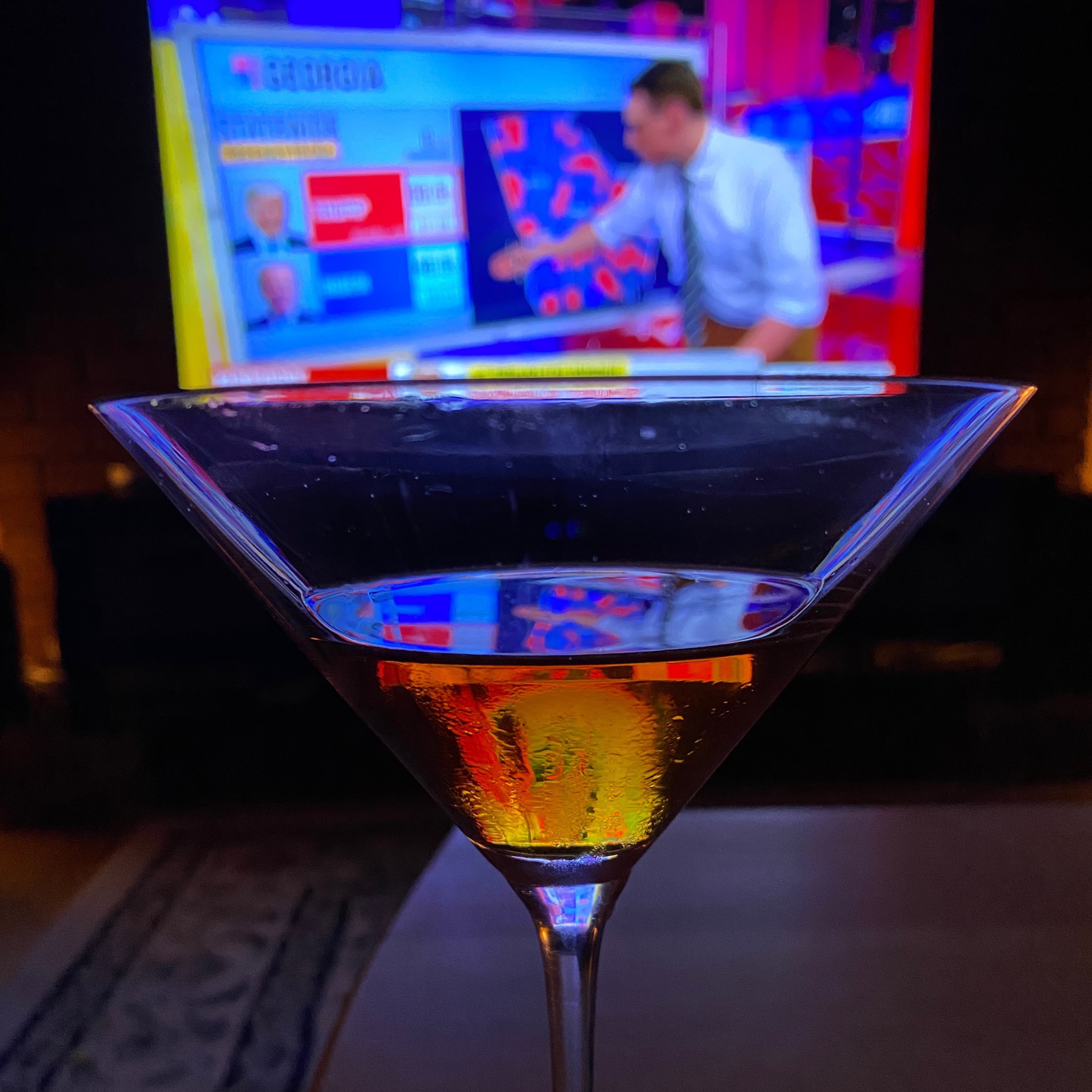 Martini glass with television in background.