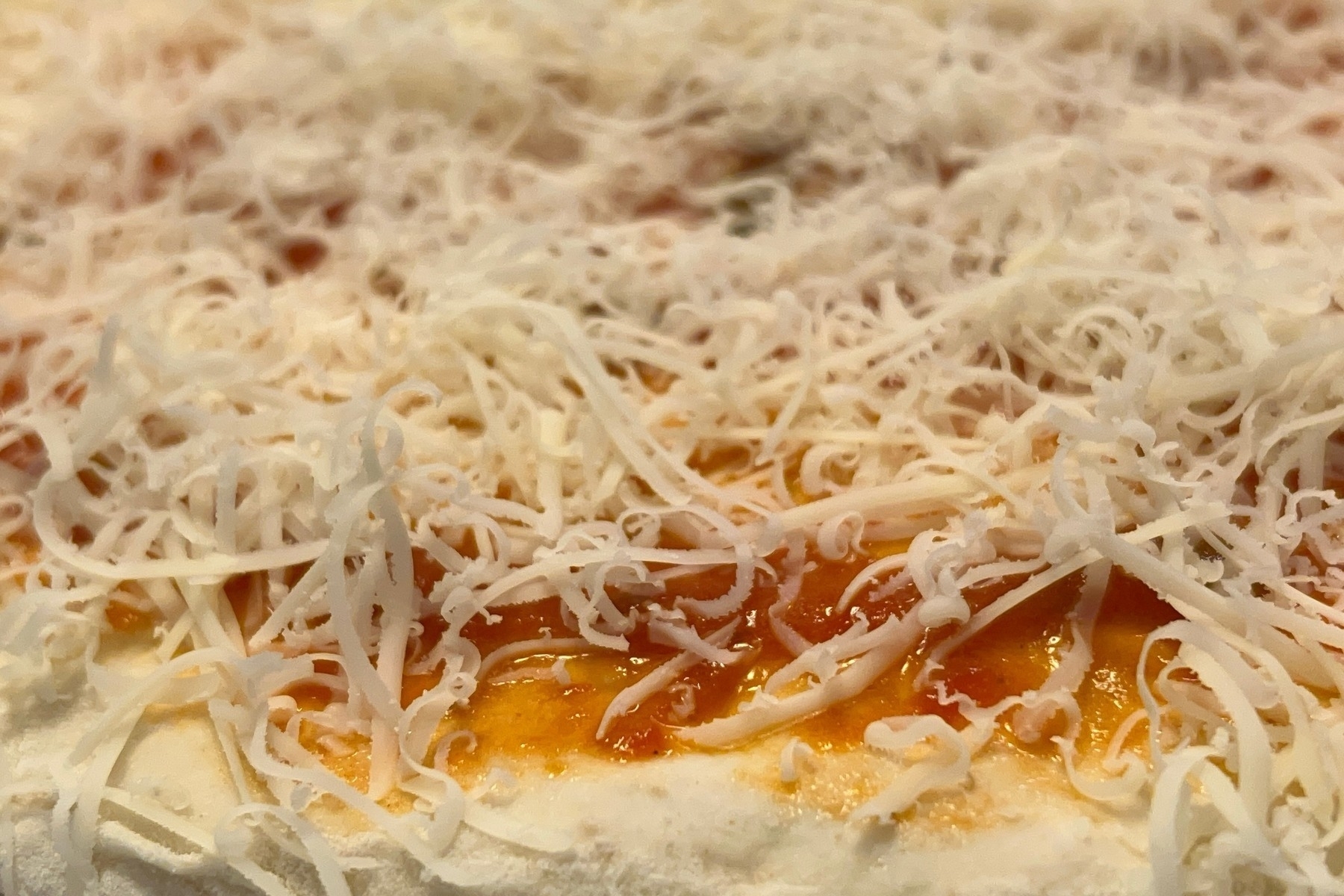 Grated Parmesan cheese on top of pizza sauce and dough before being cooked. 