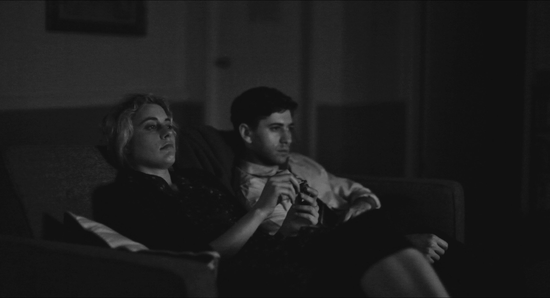 Greta Gerwig and Michael Zegen sitting on a couch watching a movie from the movie Frances Ha