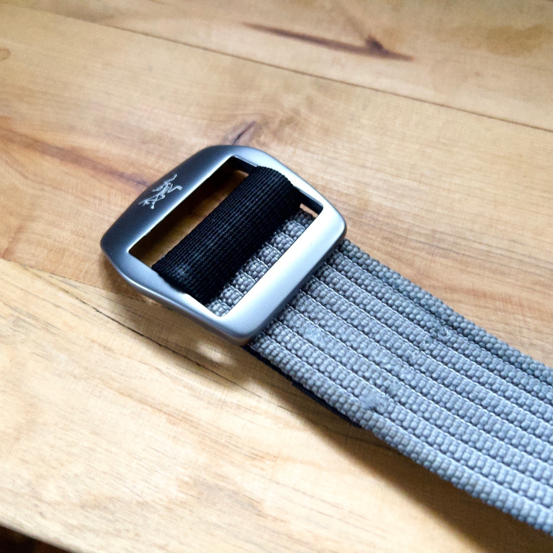 Silver buckle of men's belt with a grey woven belt. 