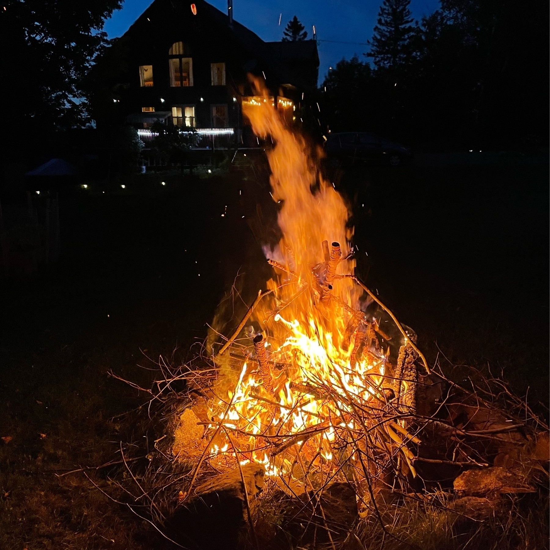 A large pile of sticks on fire in a fire pit at night with the flames rising up.