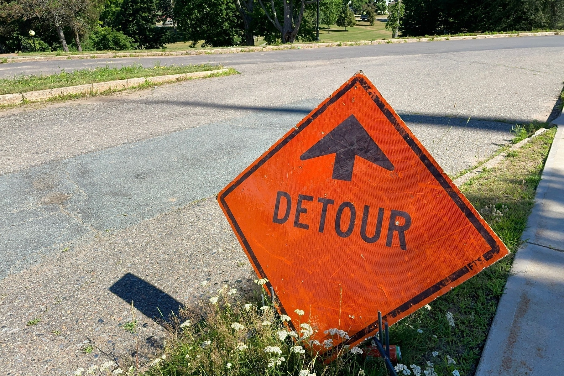 Orange detour sign resting on the grass beside a road. 