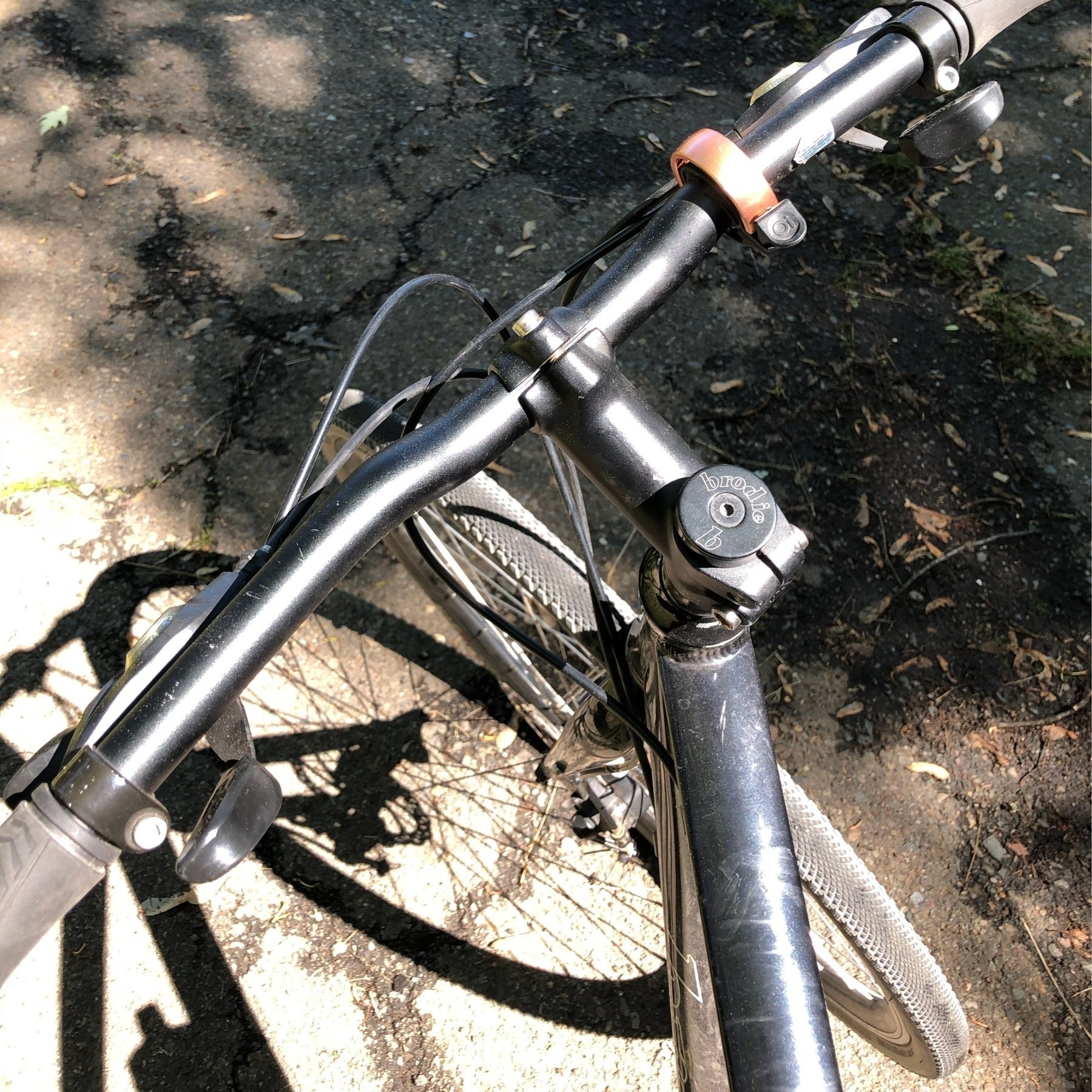 Looking down at mountain bike handlebars and front wheel of bicycle in a driveway.