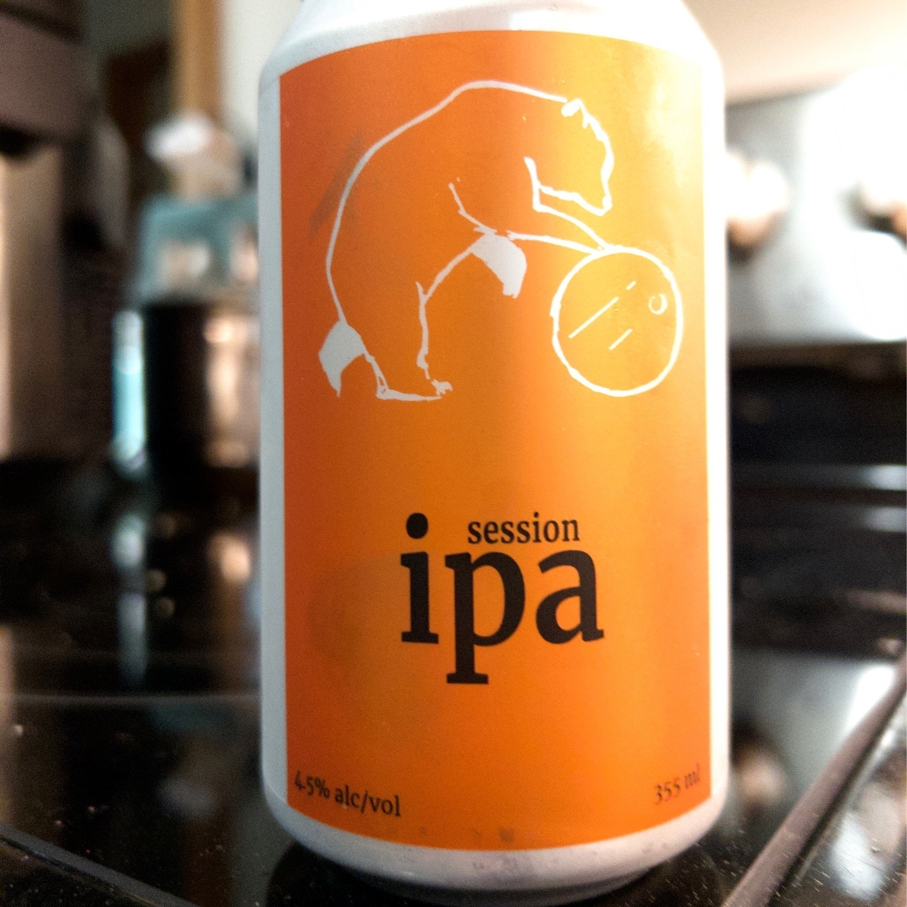 Can of beer with an orange label with a drawing of a bear rolling a barrel on the label. 