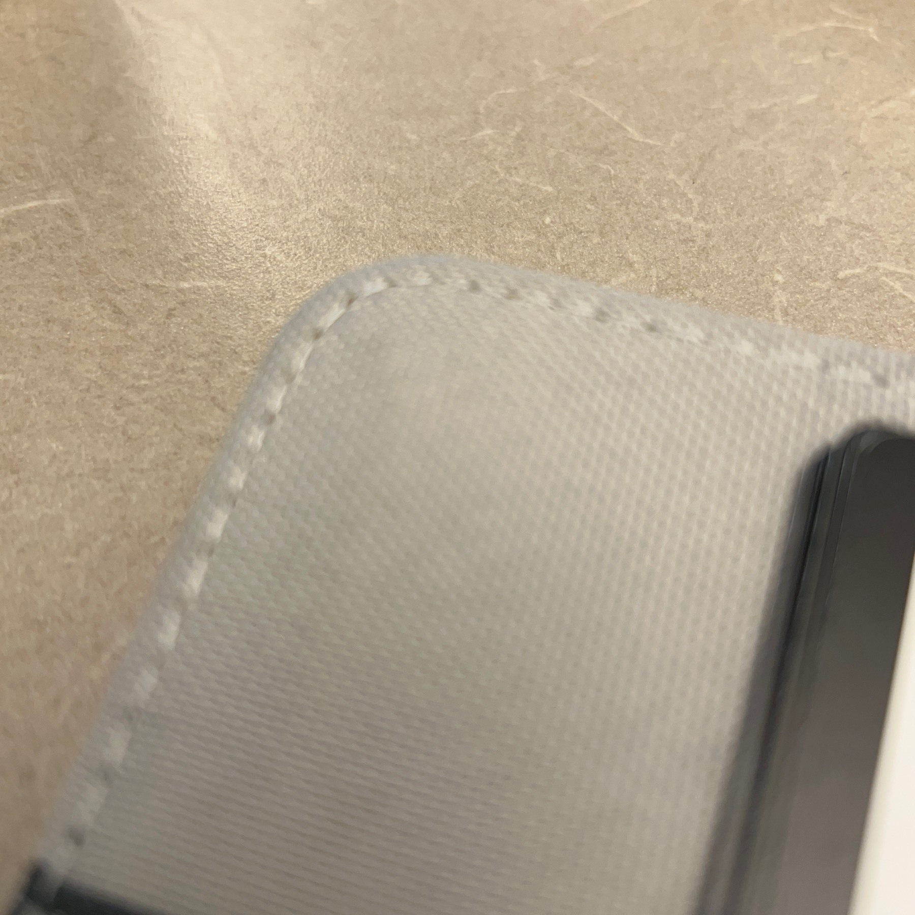 Grey stitched corner of notebook cover diagonally arranged on a grey desk. 
