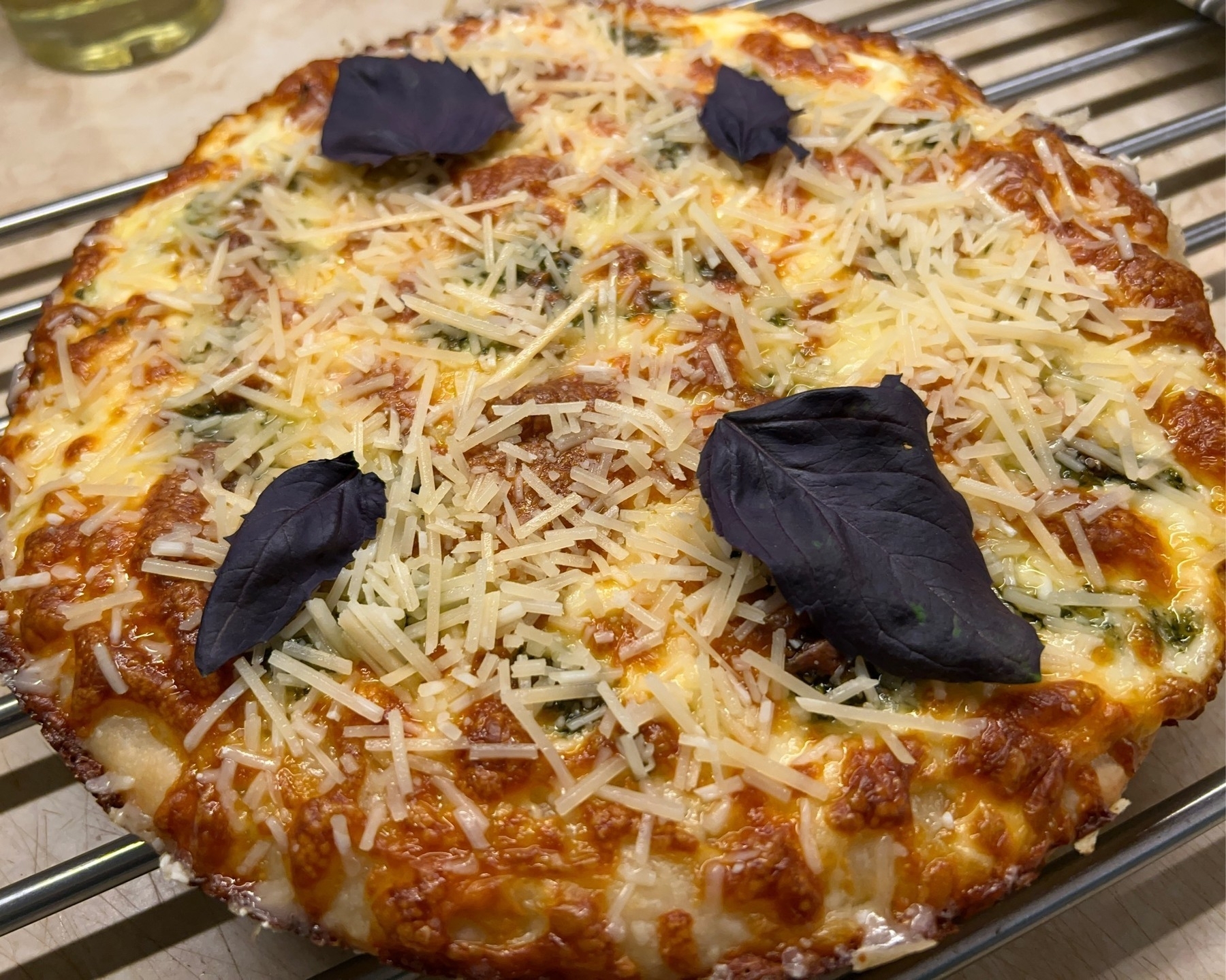 Cheese pizza cooling on a rack with red basil leaves on top. 