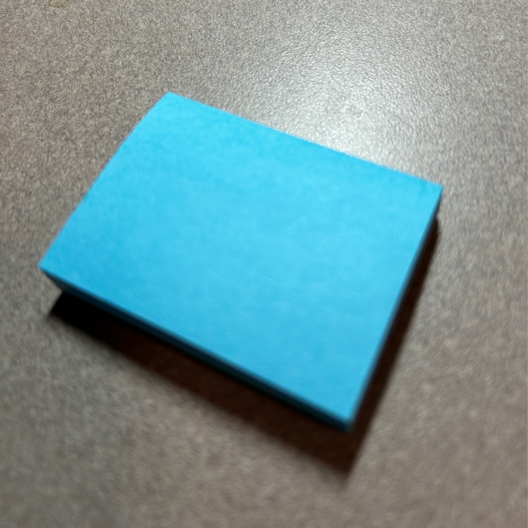 Small rectangular blue paper notepad on a grey desk. 