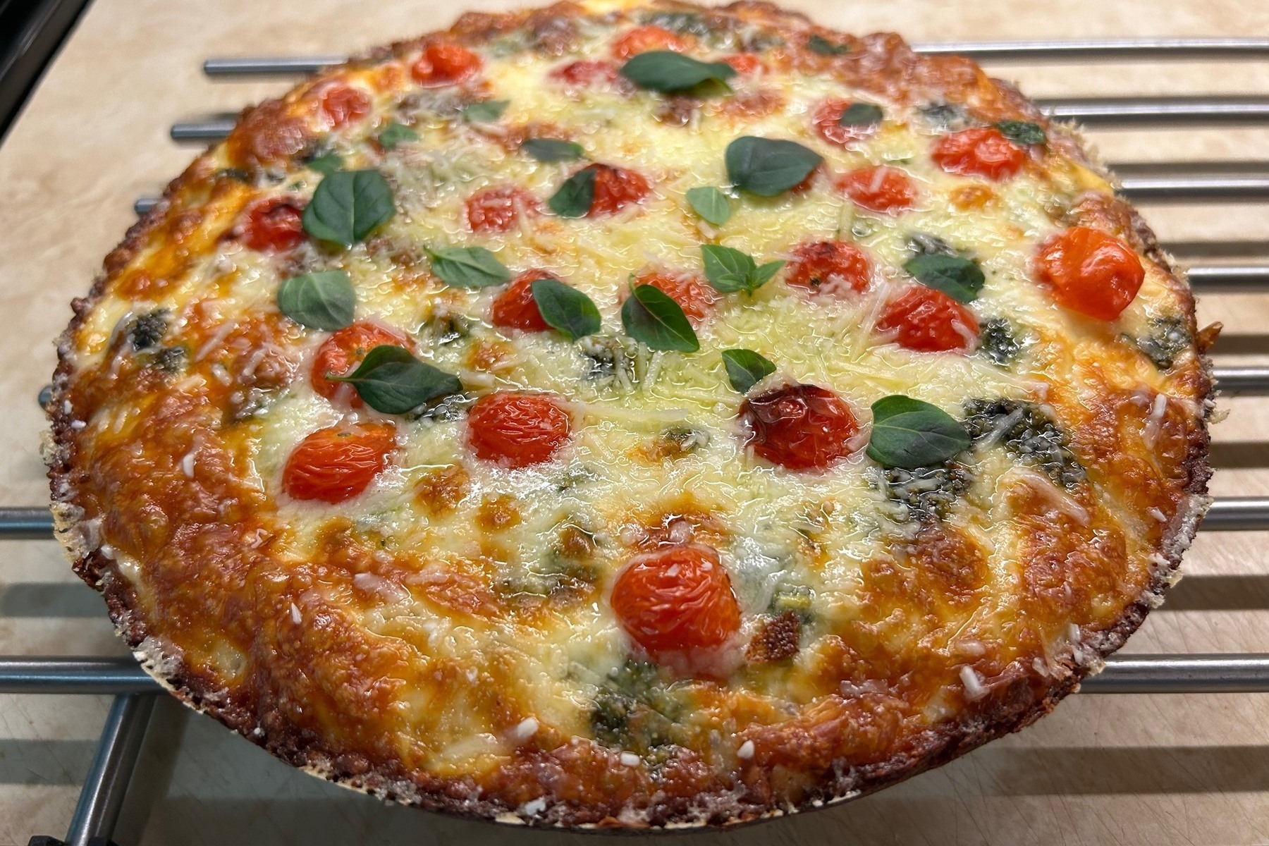 Pan pizza topped with cheese and cherry tomatoes cooling on a metal rack. 