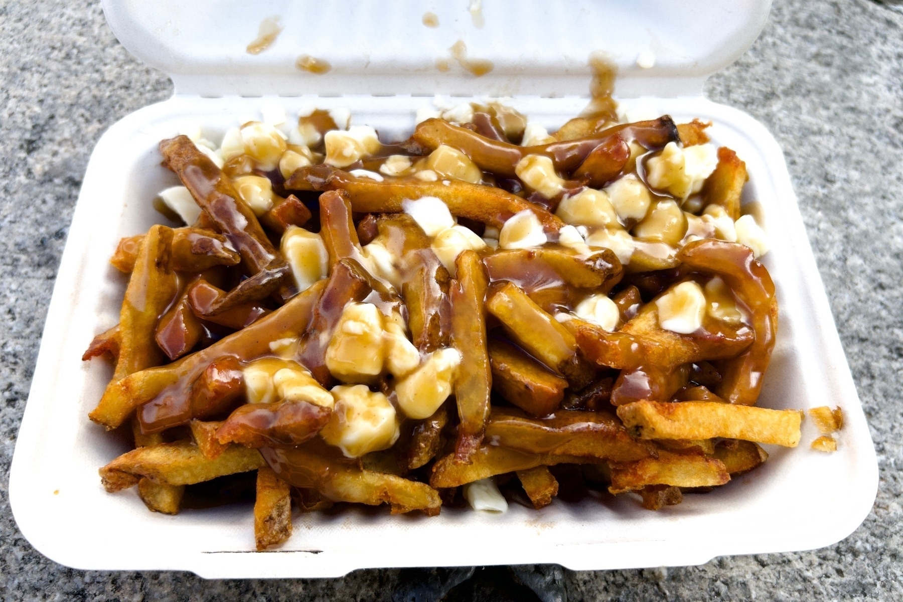 A rectangular cardboard takeout carton filled with fries covered with cheese curds and gravy. 