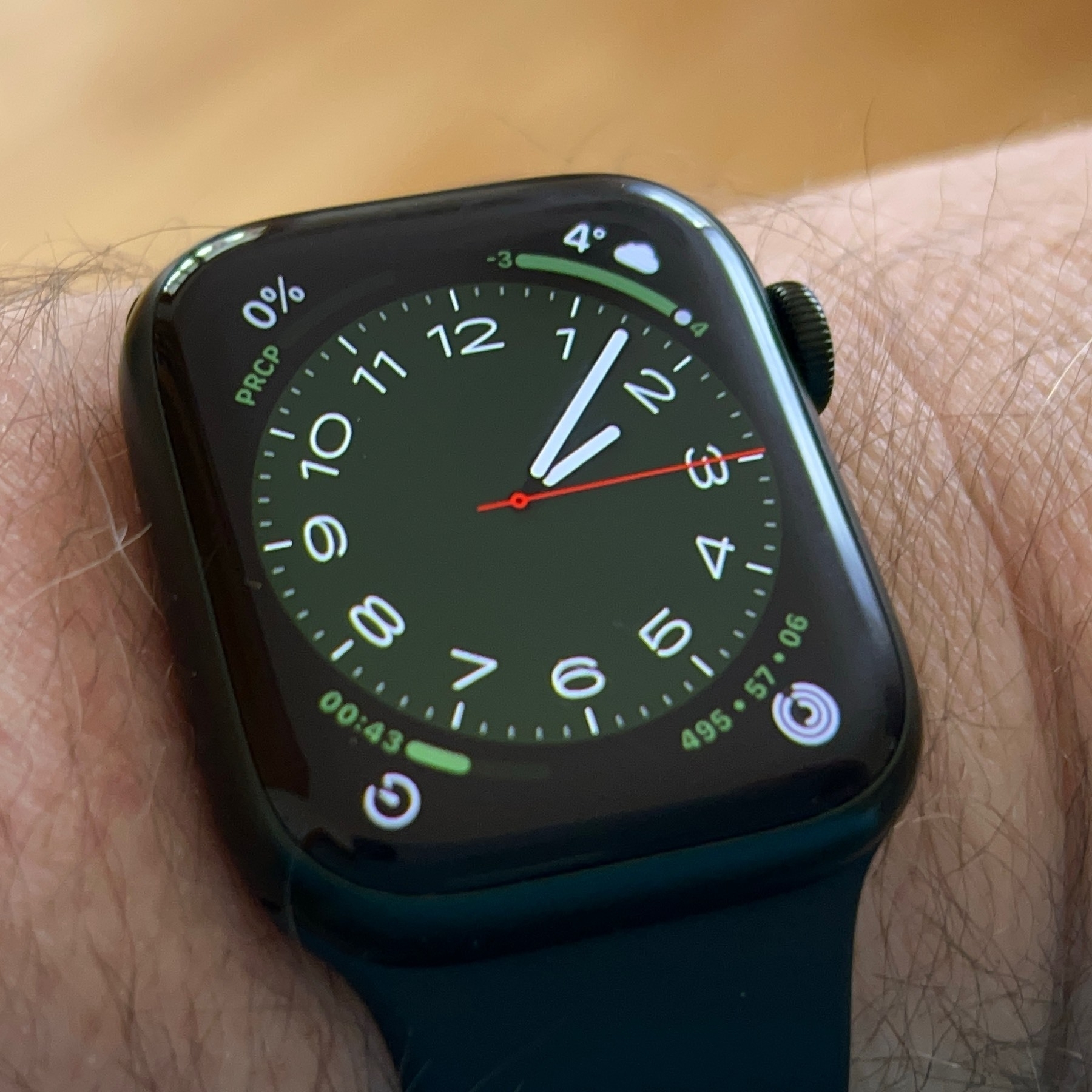 Apple Watch on wrist with an analog watch face with a black background.