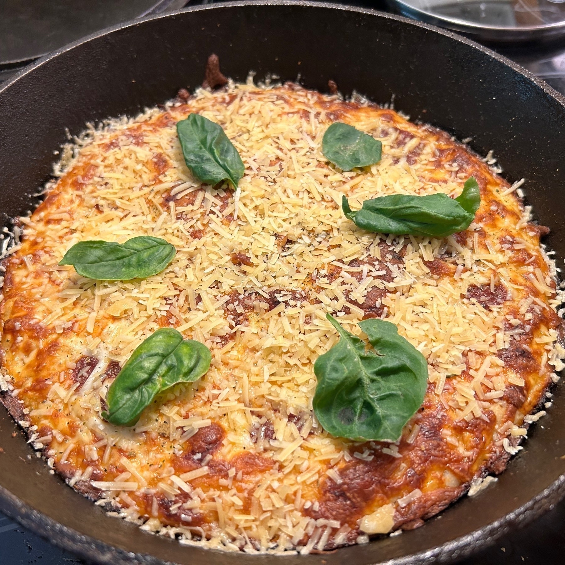 Cheese pizza in a cast iron pan with basil leaves on top in a circular pattern. 